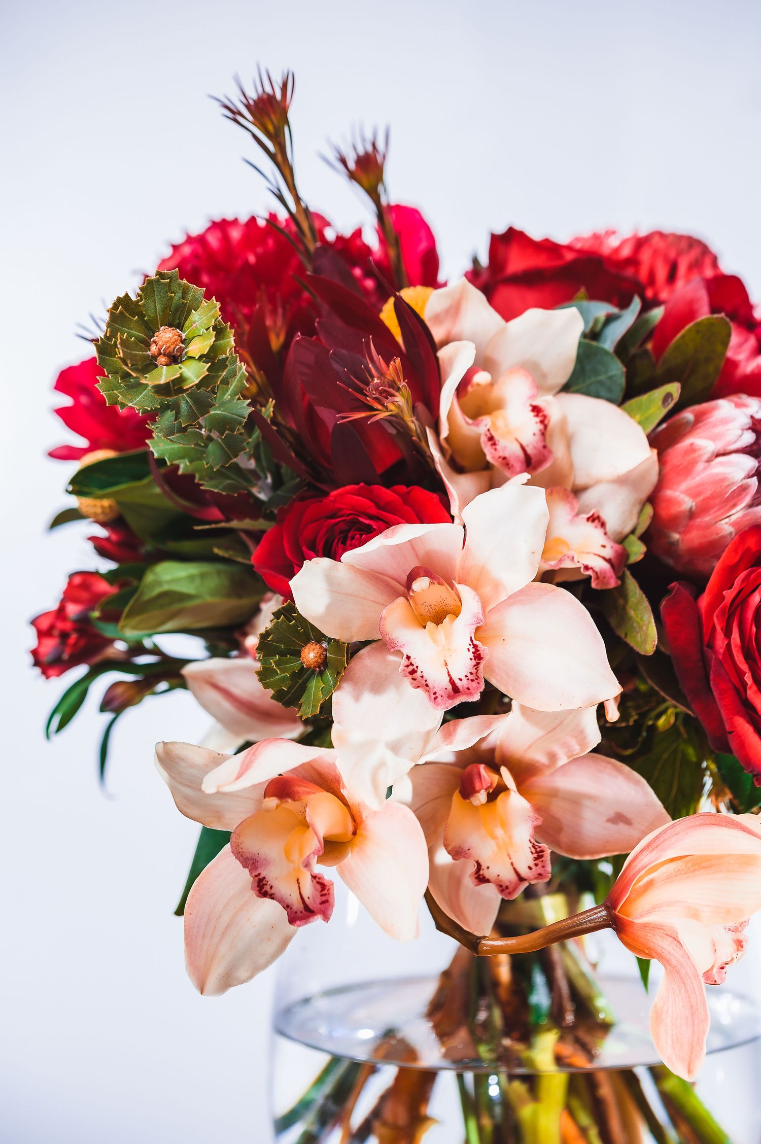 Vibrant floral arrangement with pink orchids and red roses in a clear glass vase against white background.