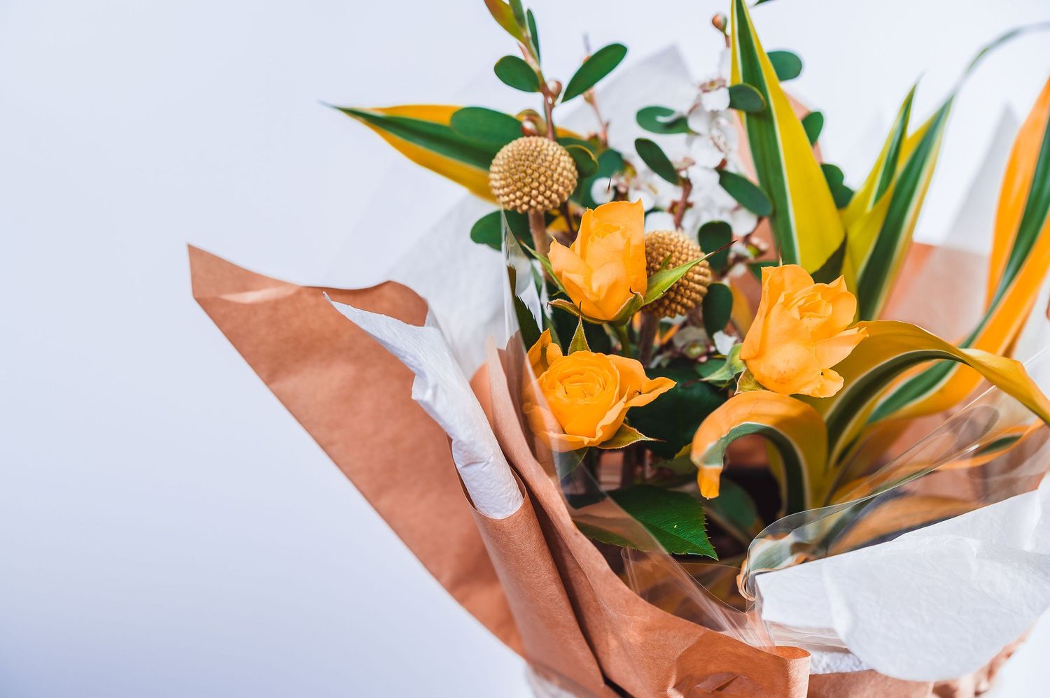 Yellow floral arrangement wrapped in brown paper with white ribbon detail.
