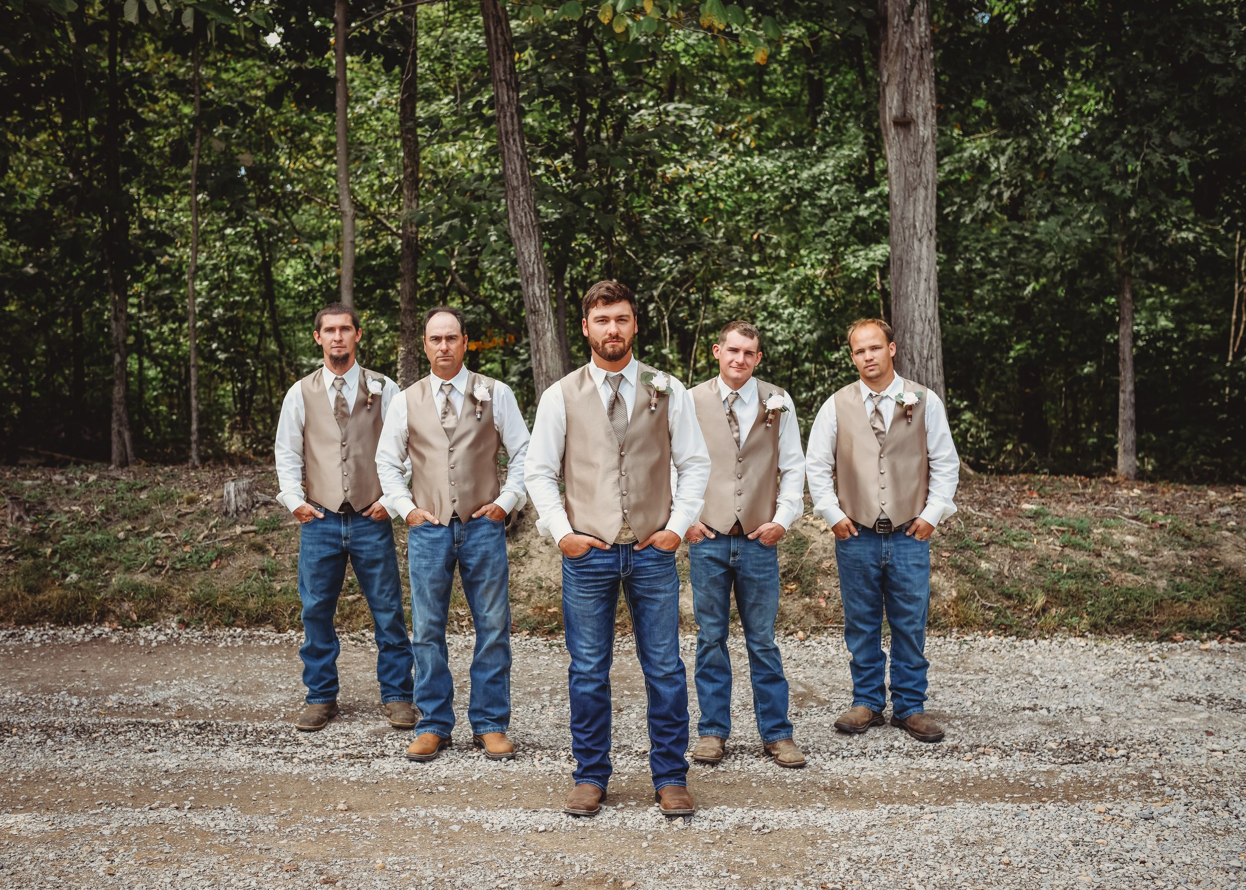 Groomsmen in jeans and light colored shirts pose casually on a gravel path.