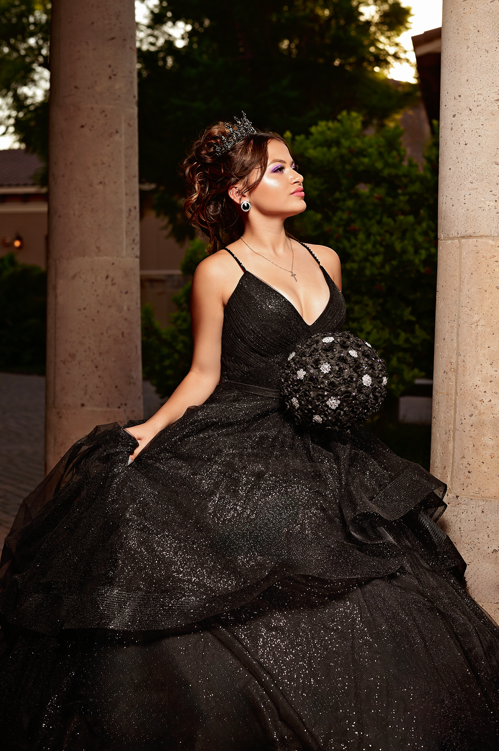 Regal portrait in a black sparkly ballgown against stone columns at sunset.