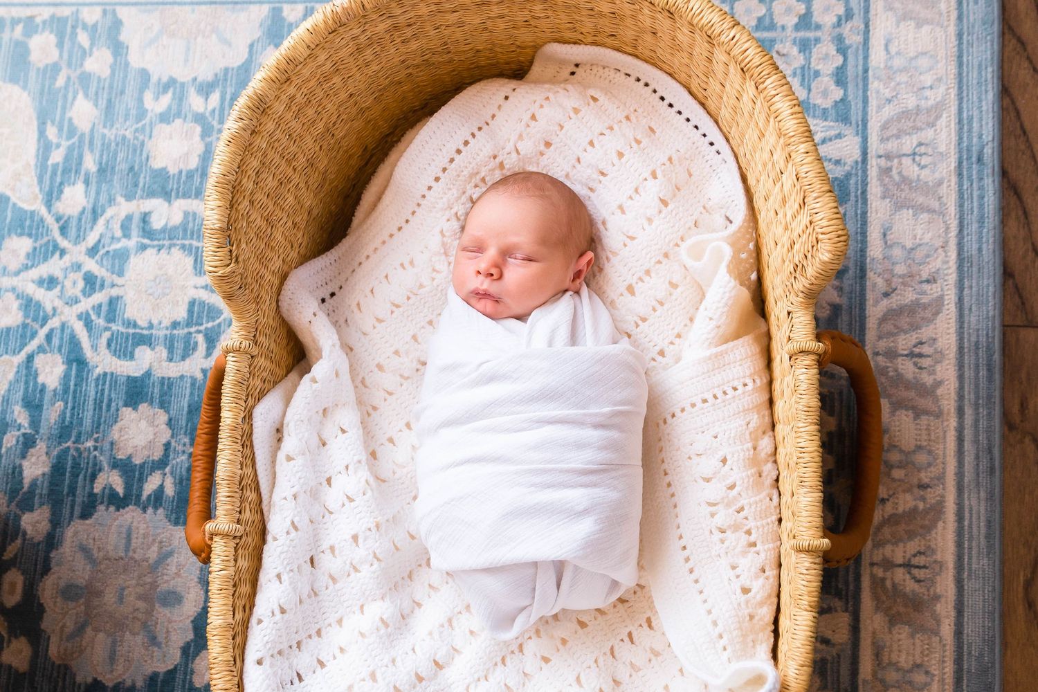 Sleeping newborn wrapped in white blanket resting in vintage wicker bassinet.