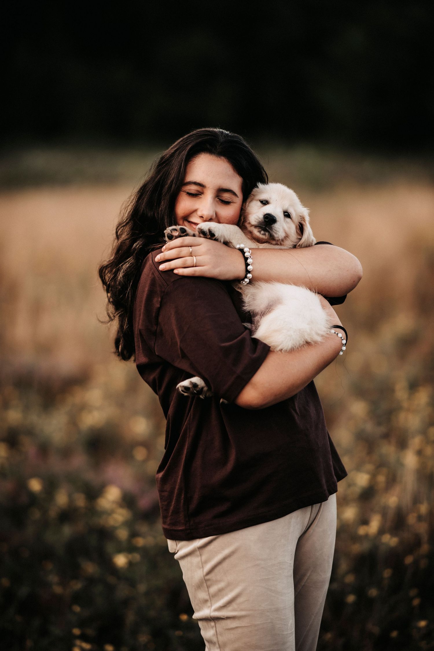 A heartwarming moment shows a person hugging their small white dog with pure joy in a field.