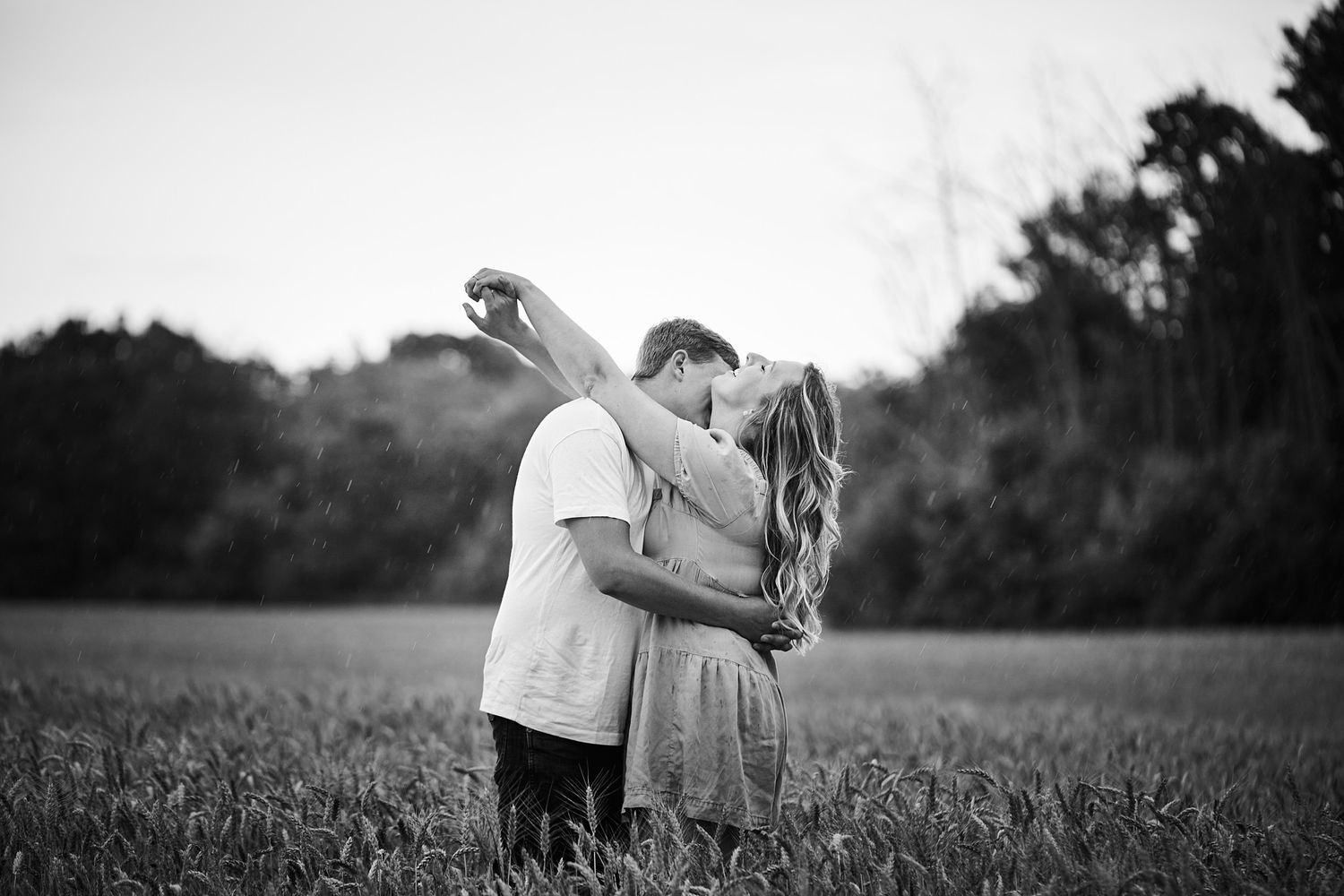 A romantic couple embracing in a pastoral field at sunset.