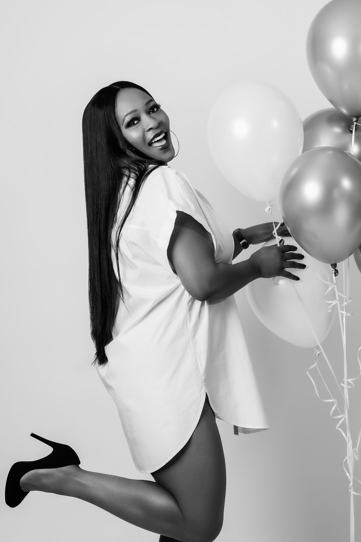 Black and white portrait of woman in white shirt posing playfully with balloons.