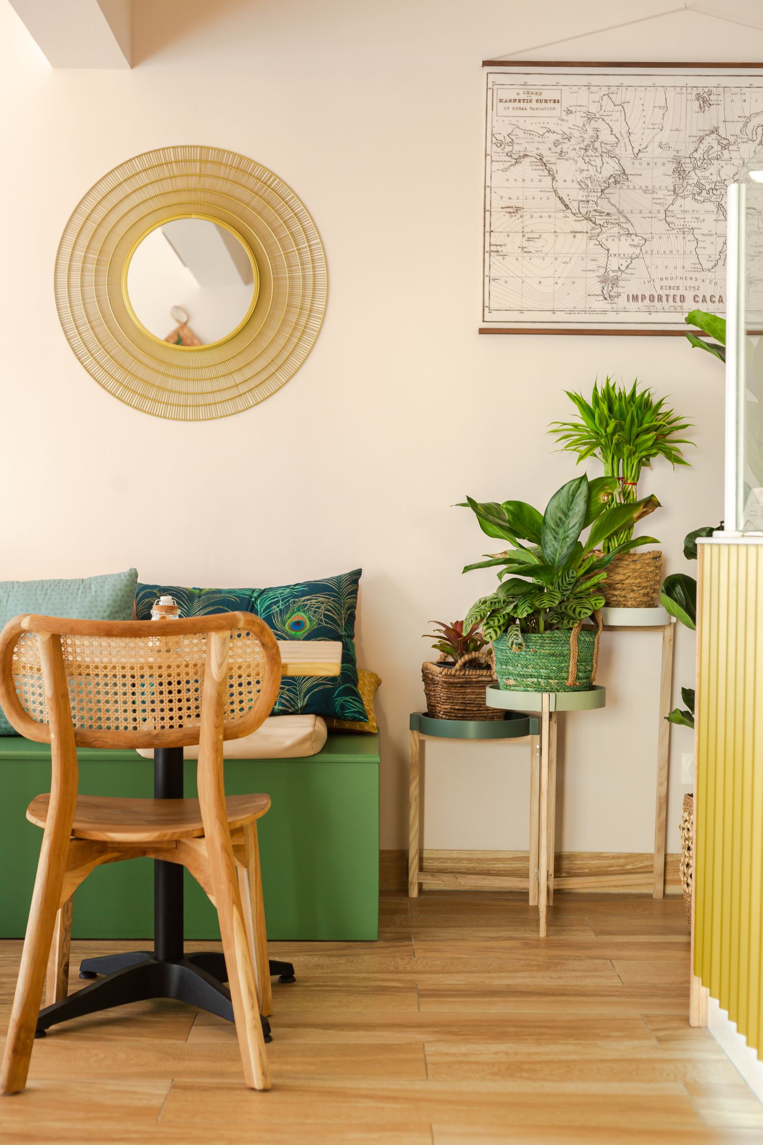 Modern interior design with rattan chairs, green accents, and vintage maps on cream colored walls.