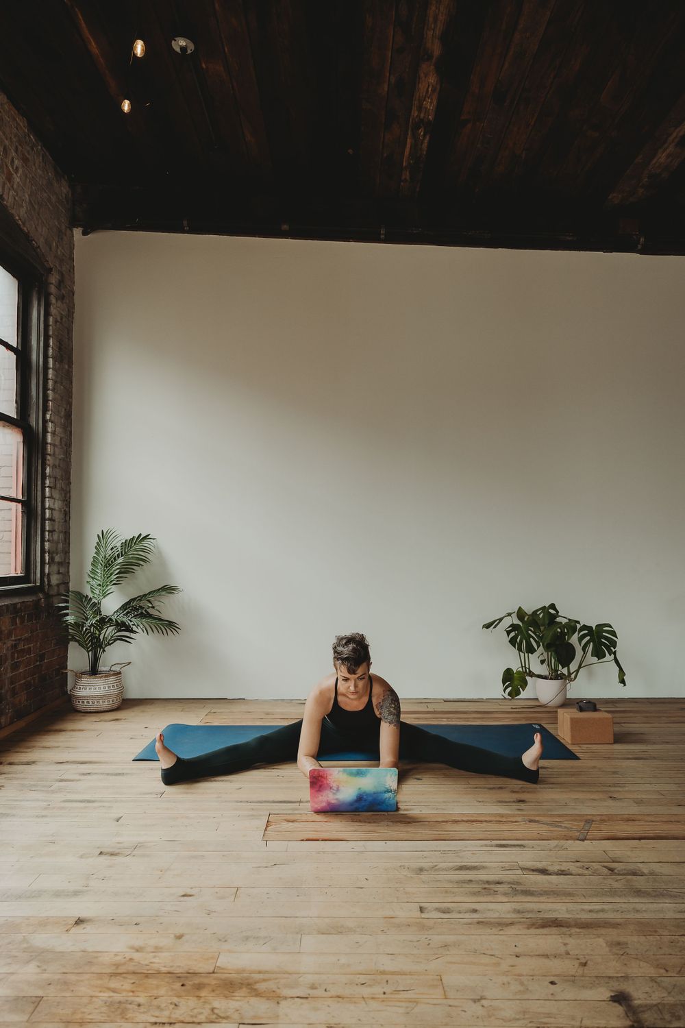 Fitness enthusiast working on laptop while doing splits on hardwood floor.
