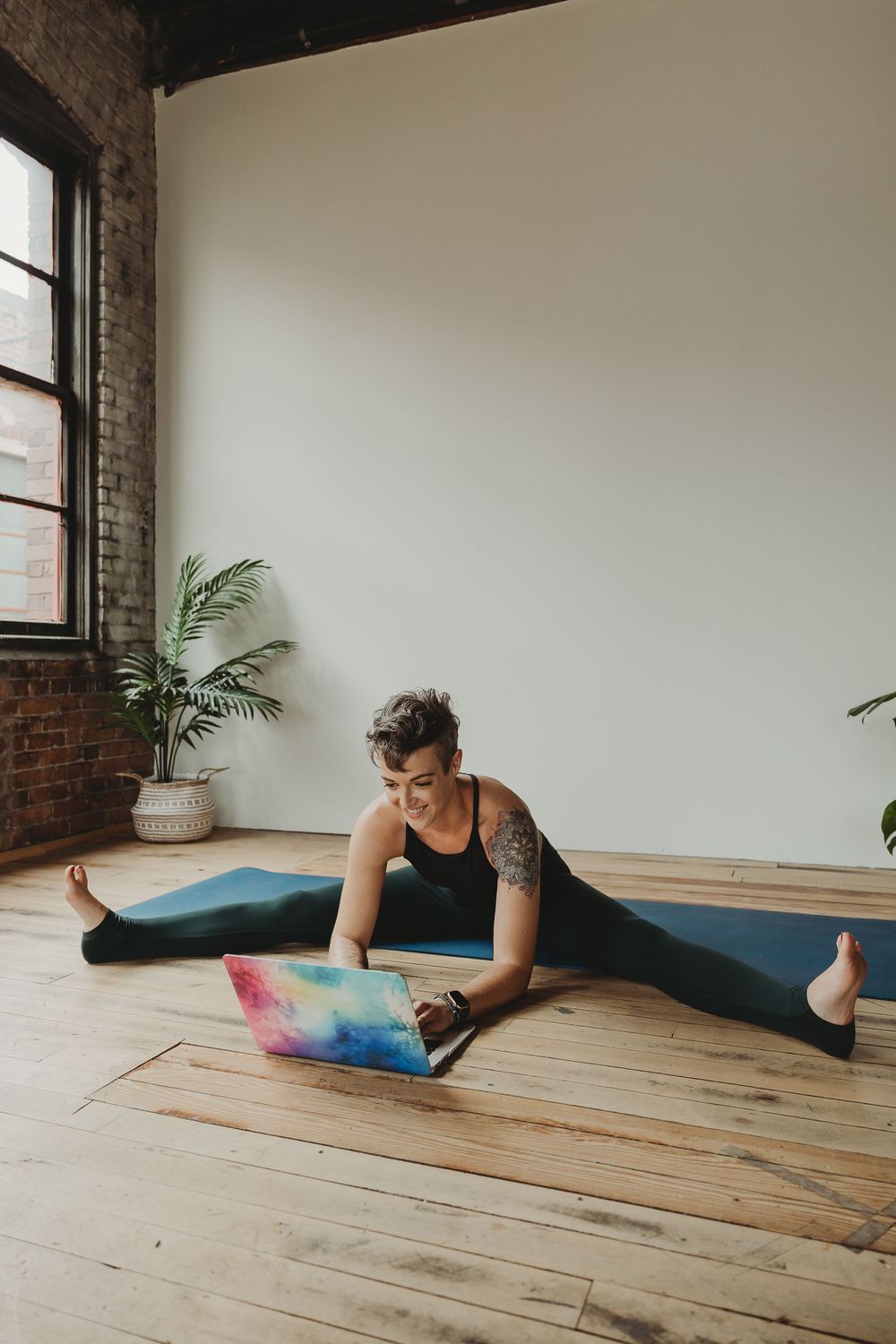 Person in active wear doing stretches with colorful laptop on wooden floor.