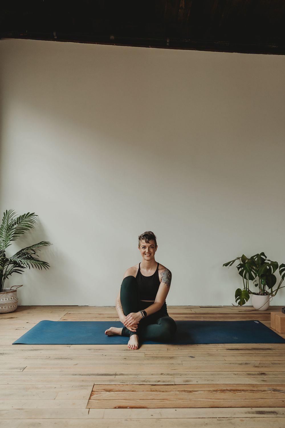 Yoga practitioner sitting on blue mat in minimal studio setting.