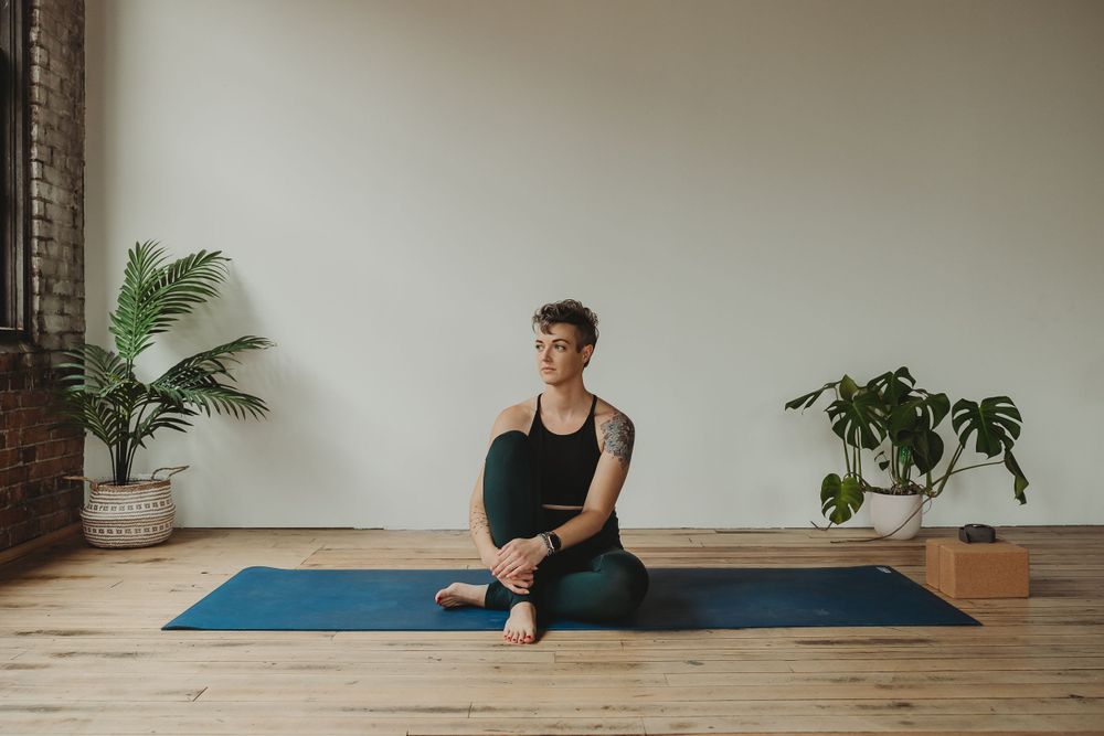 Fitness instructor seated on blue yoga mat in minimalist studio space.