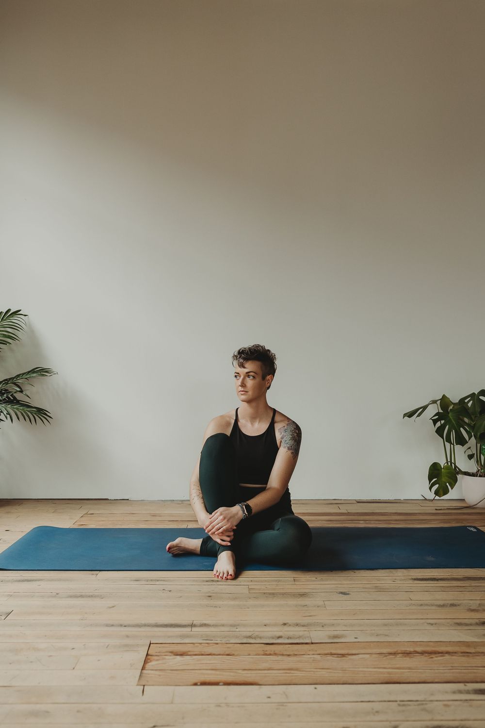 Yoga instructor in relaxed seated pose on blue mat against white wall.