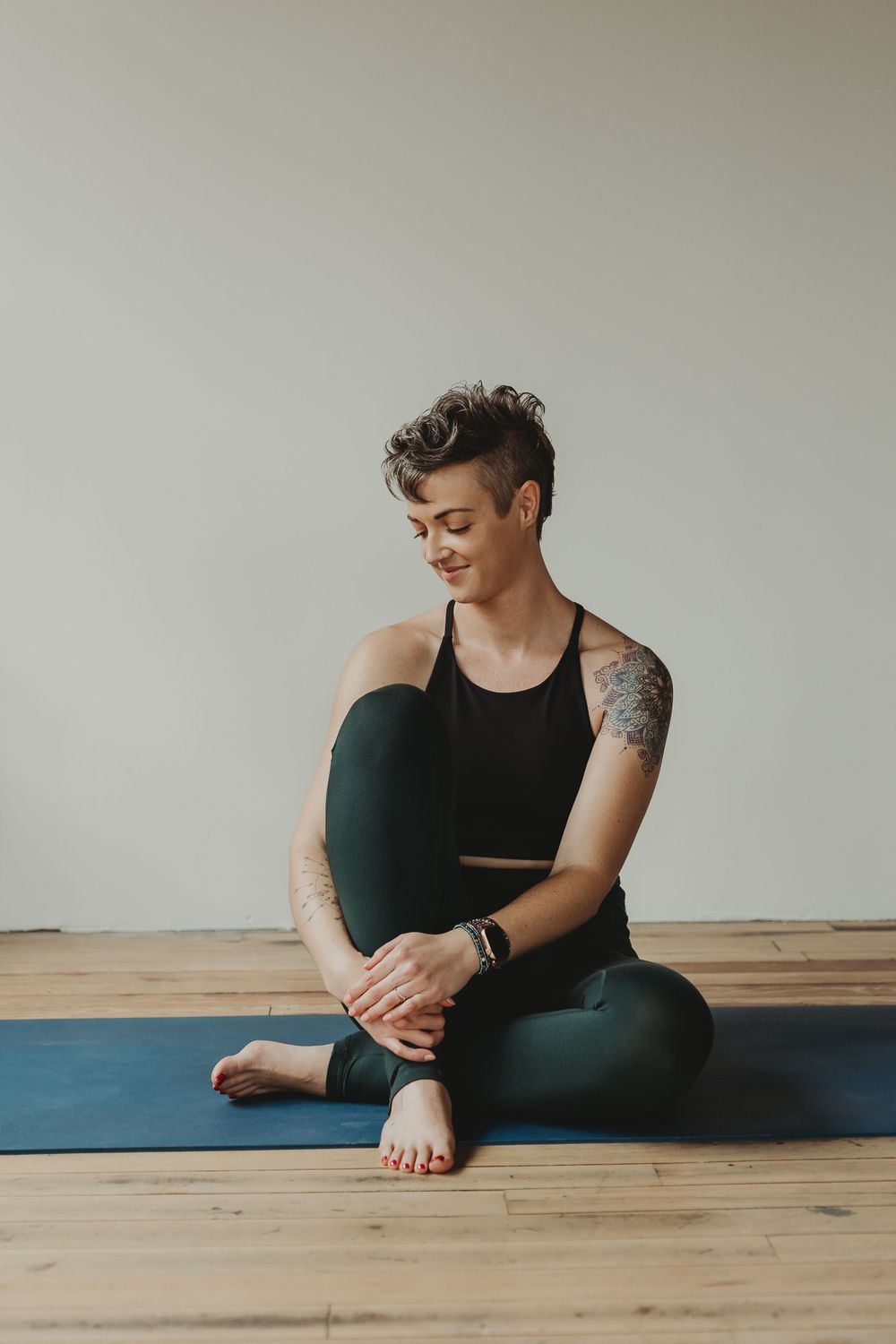 Athletic person in black workout attire sitting cross-legged on blue yoga mat.