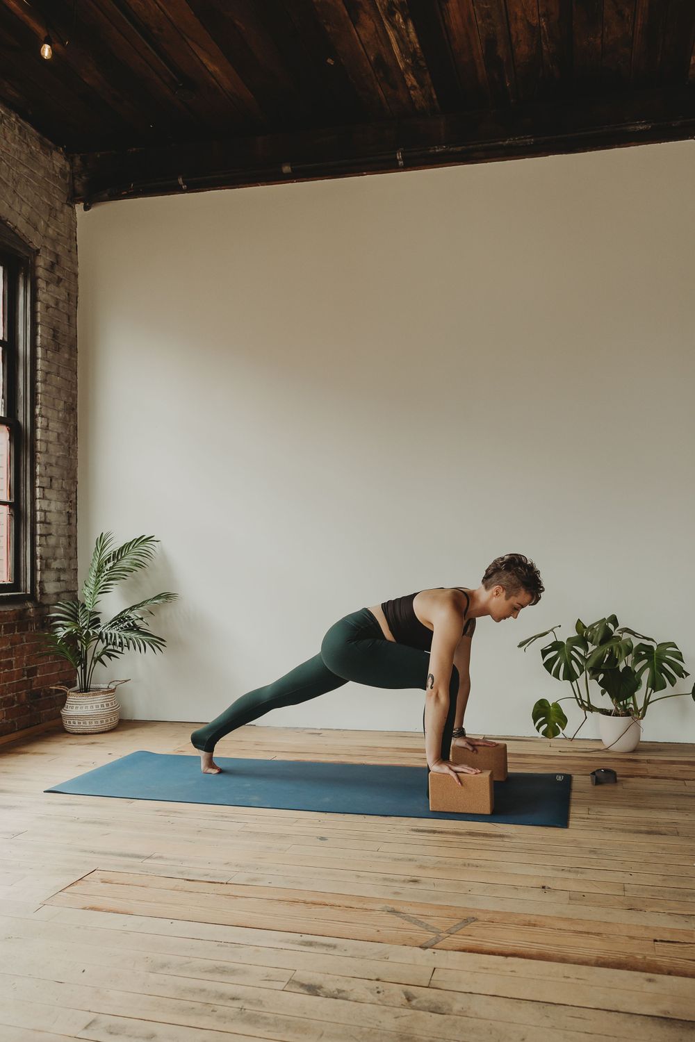 Demonstration of a plank pose variation using a wooden yoga block in a sunlit studio with hardwood floors.