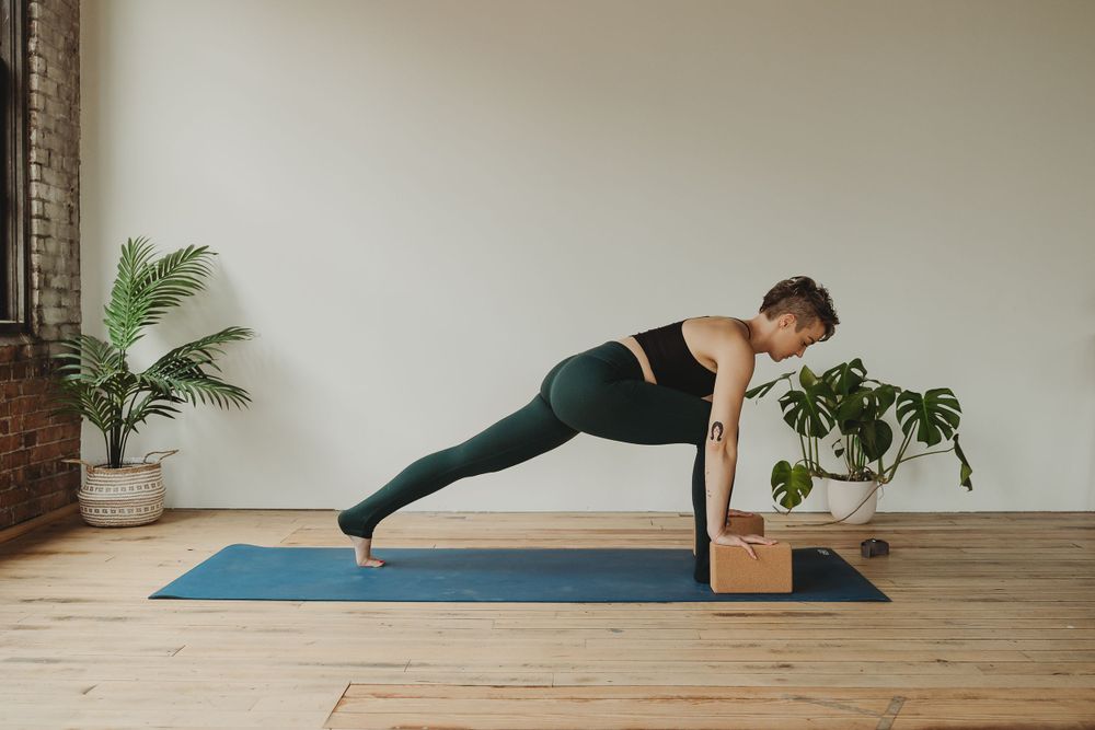 Side plank pose being demonstrated on a blue yoga mat with a wooden block for support.