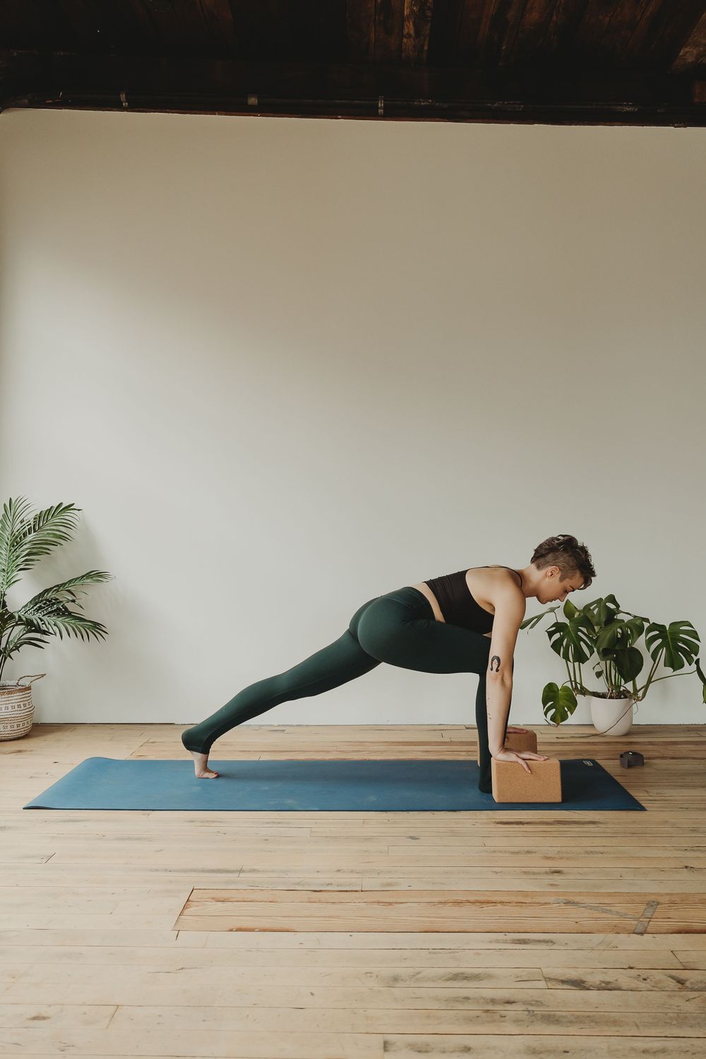 Advanced yoga pose showing plank variation with wooden block support in a minimalist studio setting.