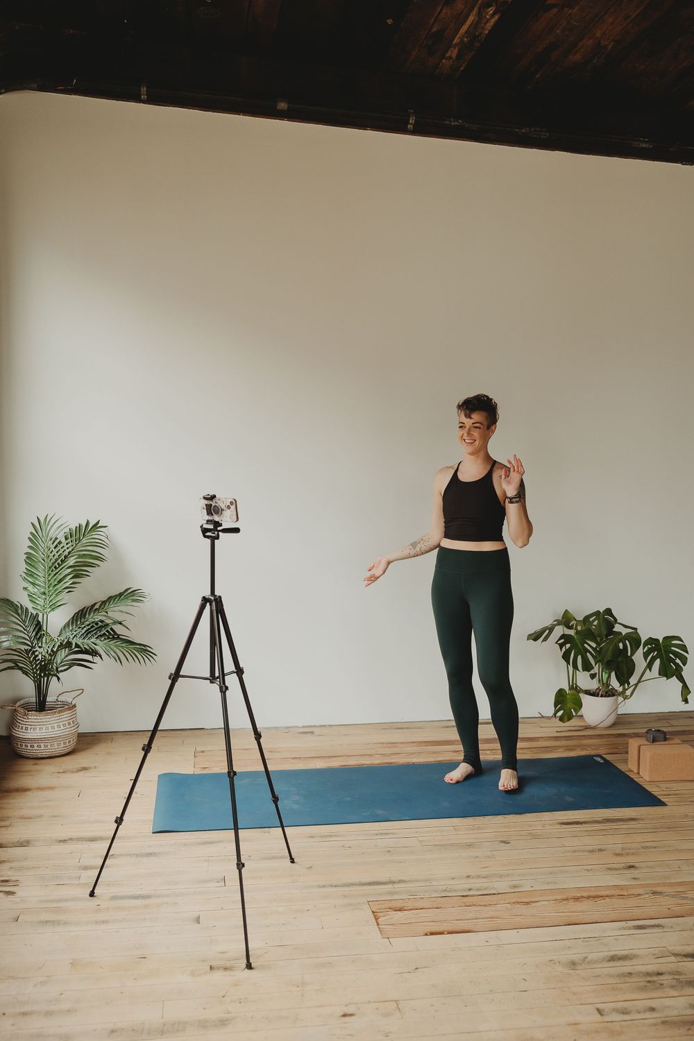 Yoga instructor filming content with camera on tripod in minimalist studio with hardwood floors.
