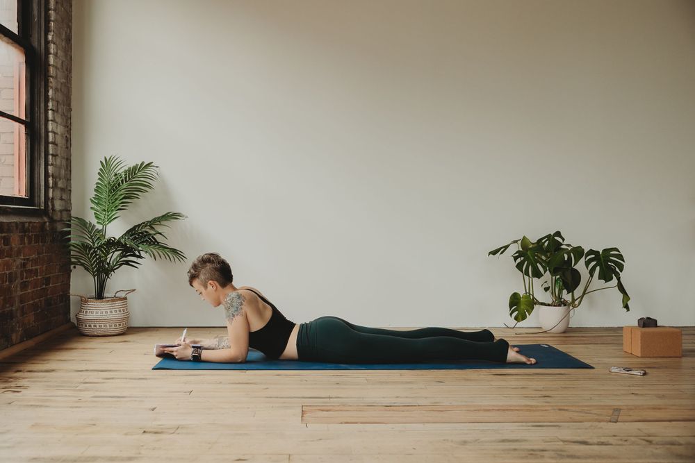 Yoga practitioner in prone position on blue mat reviewing content on mobile device.