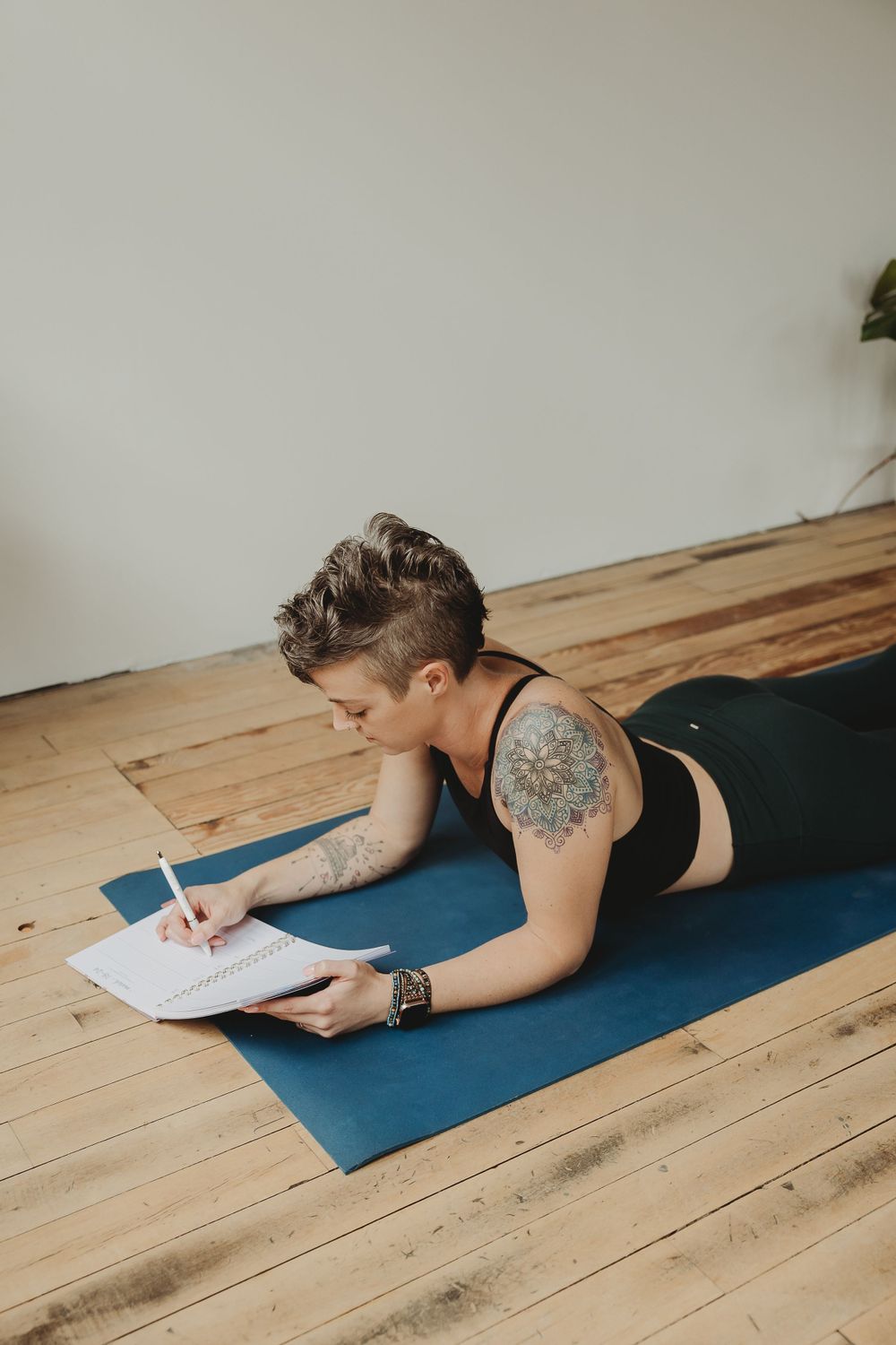 Individual journaling on yoga mat in serene room with wooden floors and white walls.