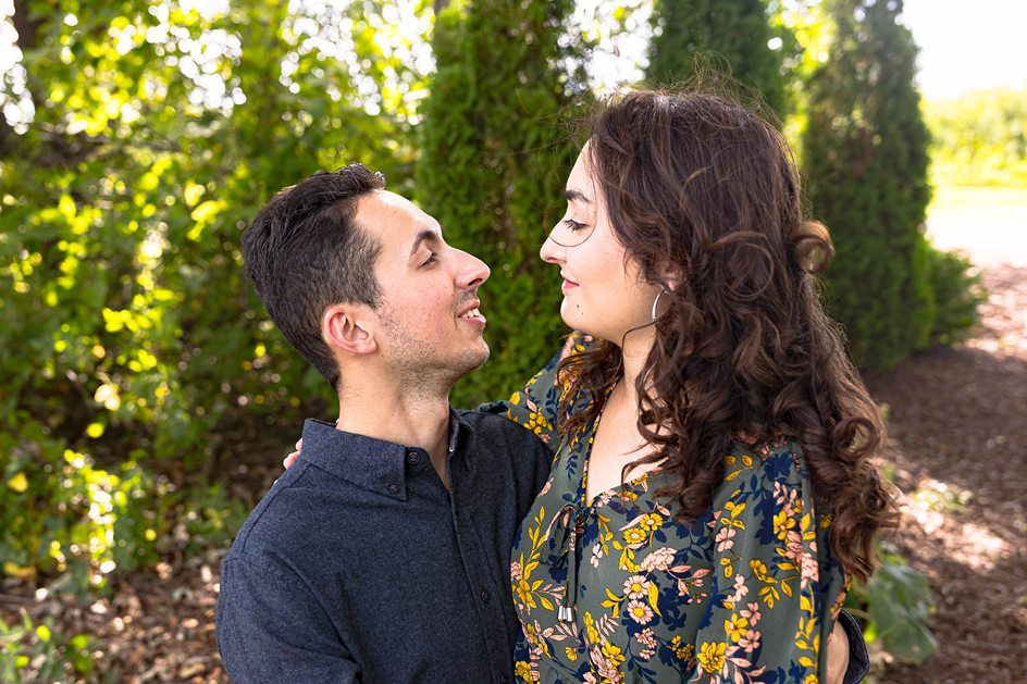 A romantic couple shares an intimate moment on a sunlit garden path among green foliage.