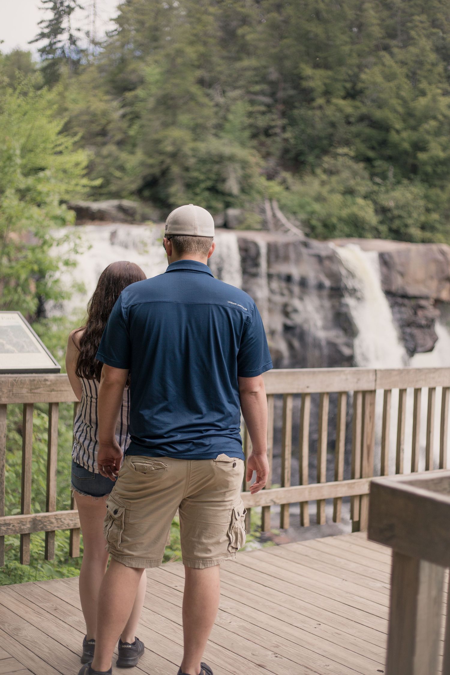 Couple admiring scenic waterfall view from wooden observation deck.