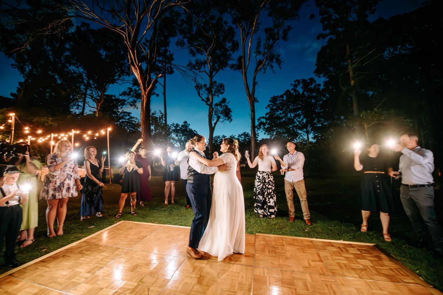 Couple shares first dance on outdoor dance floor surrounded by guests with sparklers.