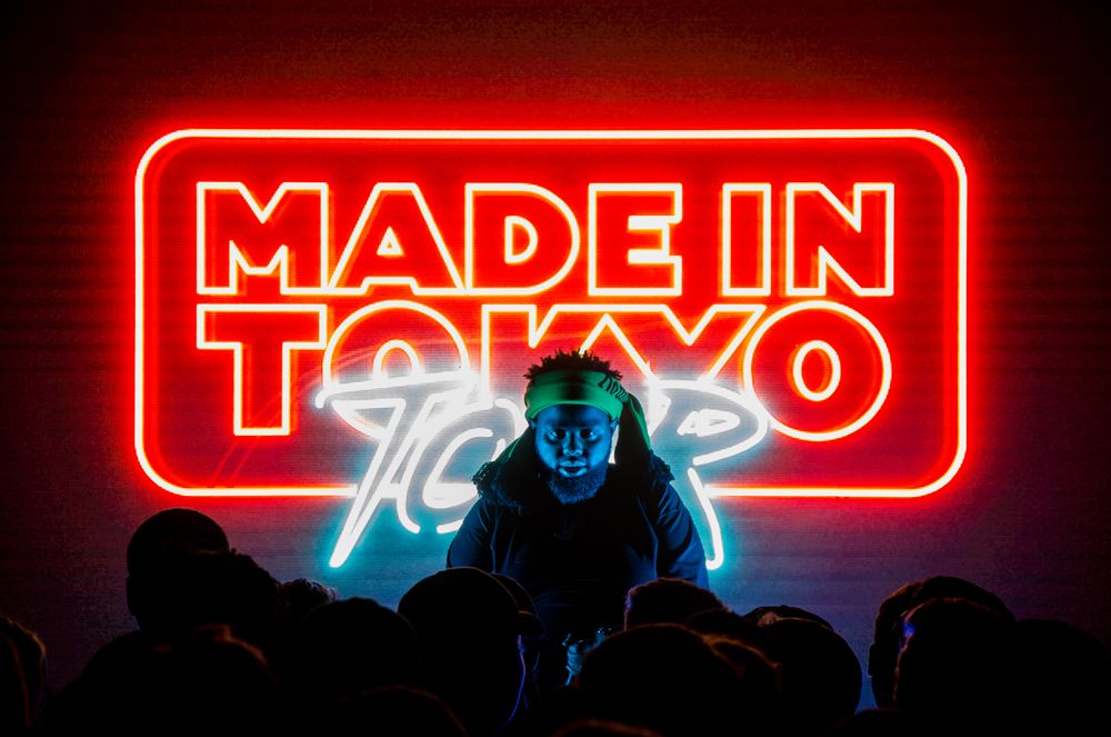 R&B artist 24 HRS sits in front of a neon made in tokyo tour sign at a concert in rhode island