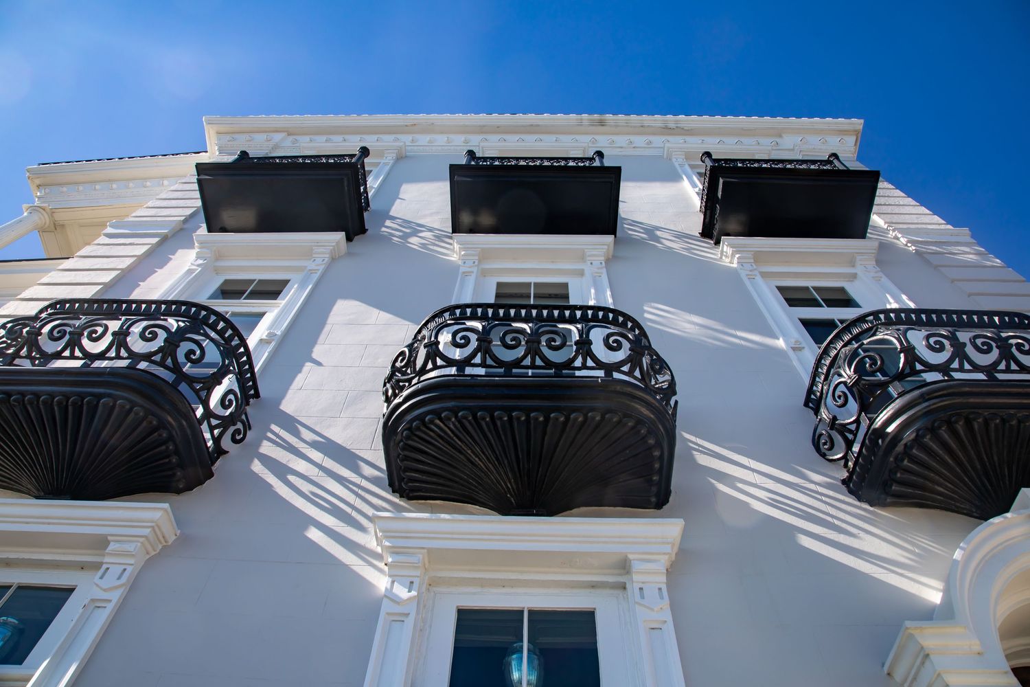 Three ornate black iron balconies on white classical building facade against blue sky.