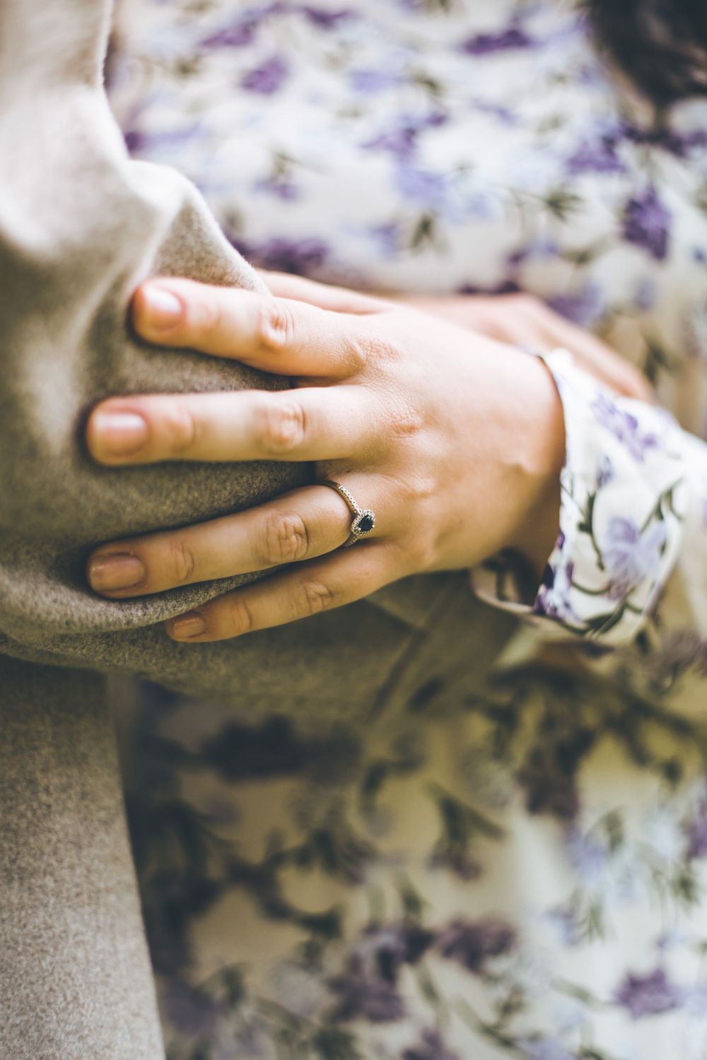 Close-up of hands showing engagement ring against floral fabric background.