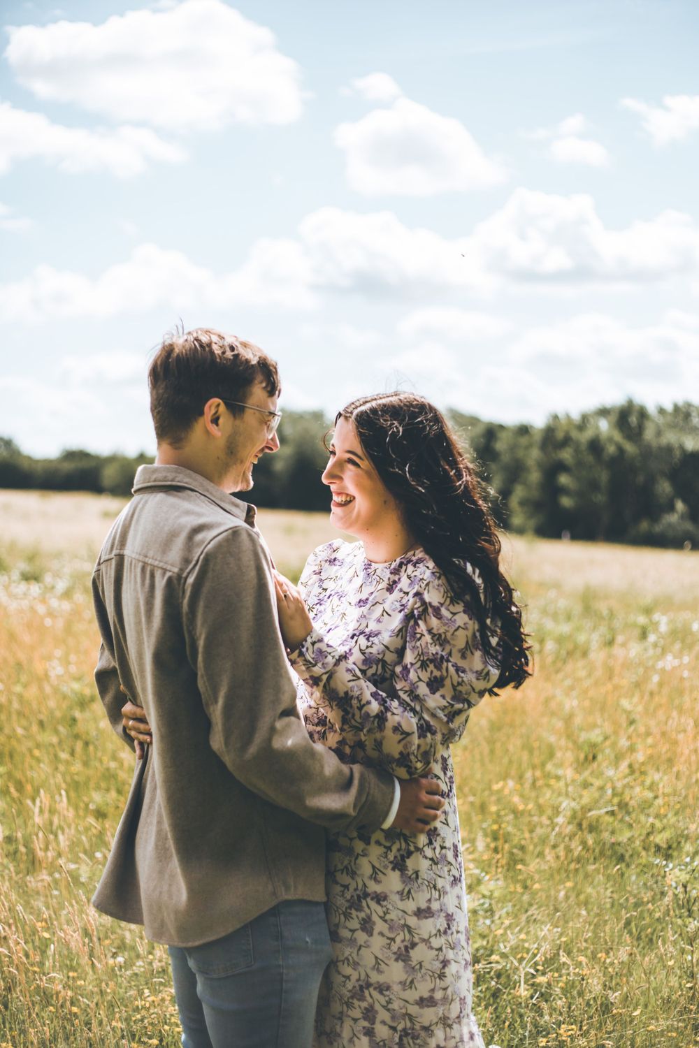 Playful couple shares laughter in a sun-filled meadow.