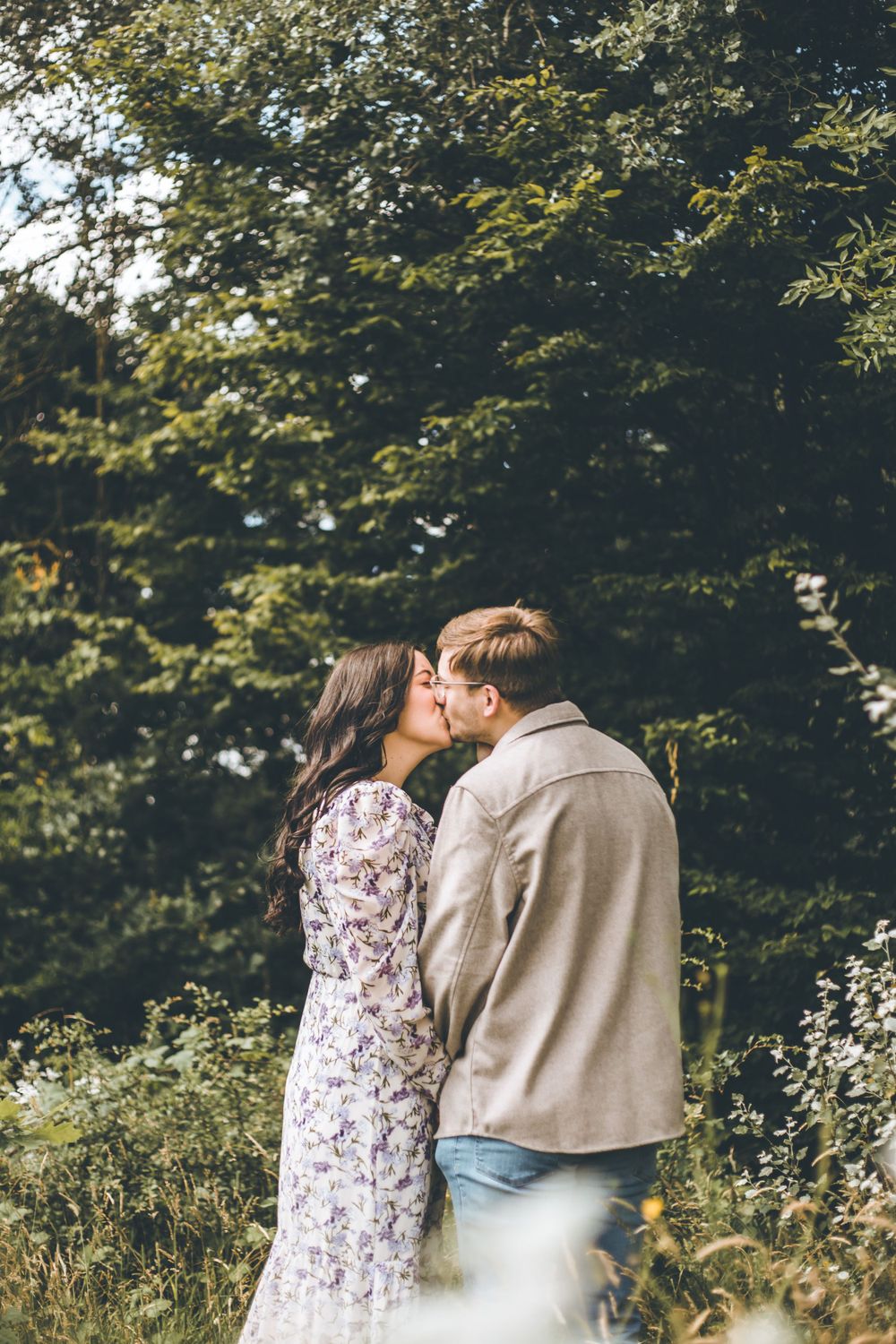 A romantic couple sharing a tender kiss among green trees in nature.