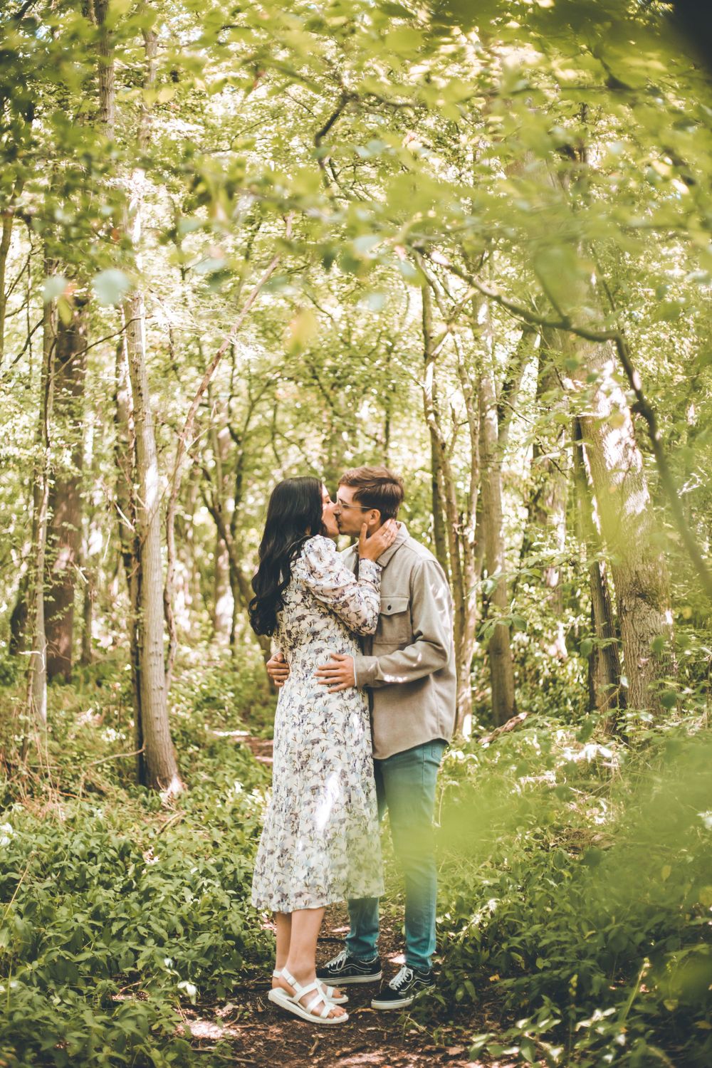 A couple sharing an intimate moment on a forest path surrounded by trees.
