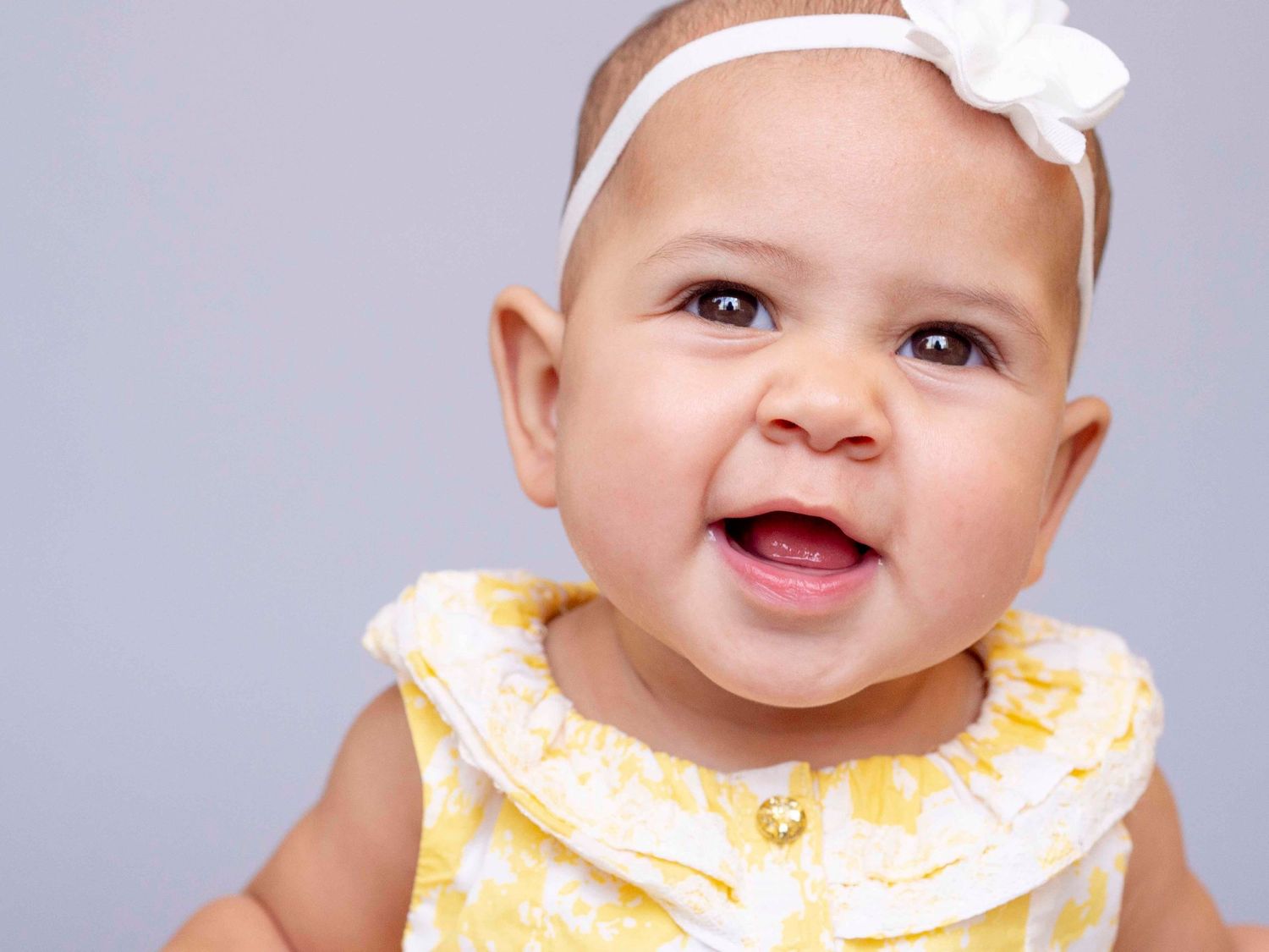 Baby girl with bow and cute smile, solid grey background