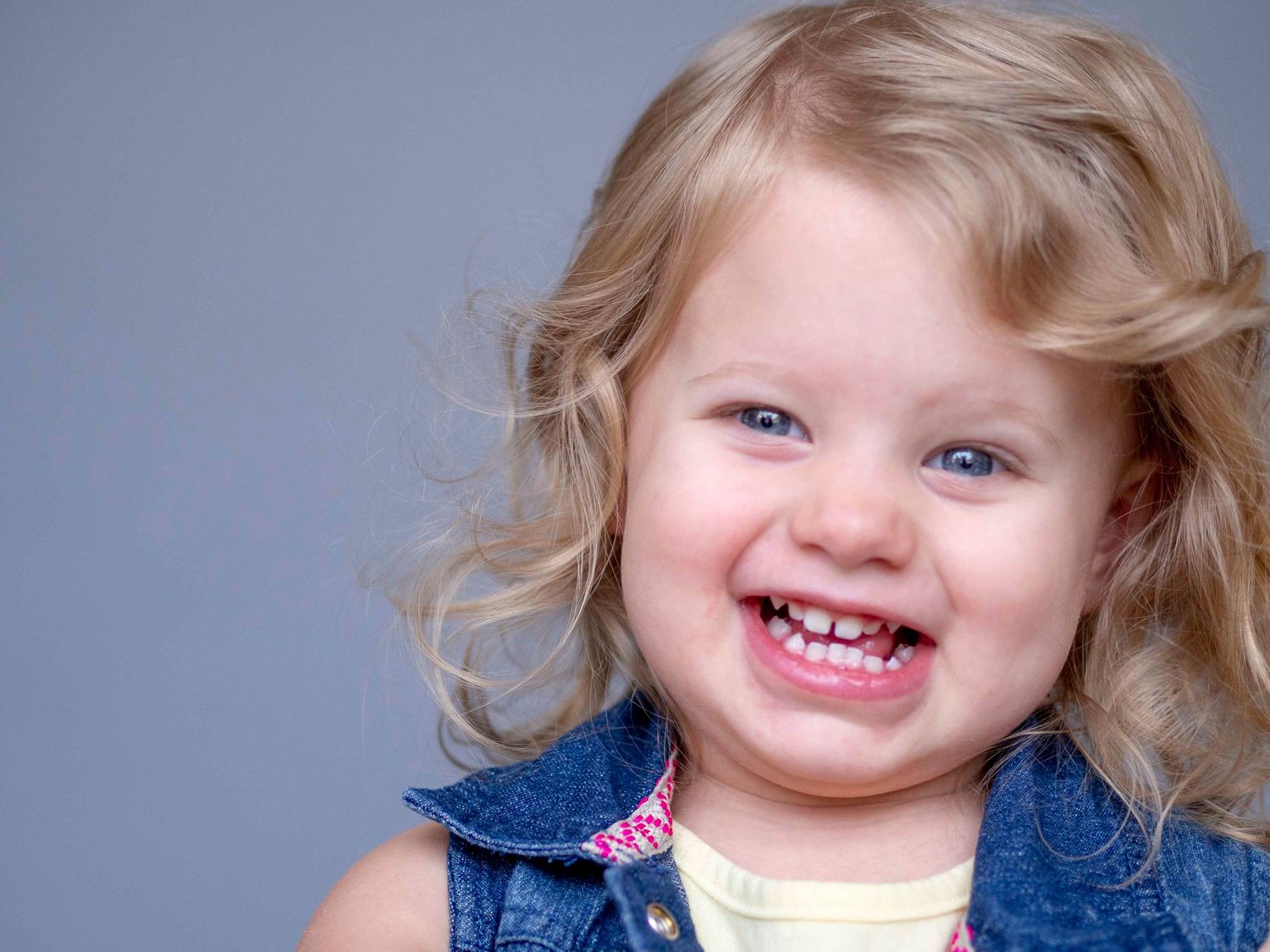 Pre-school aged girl, cute toothy smile, solid grey background.