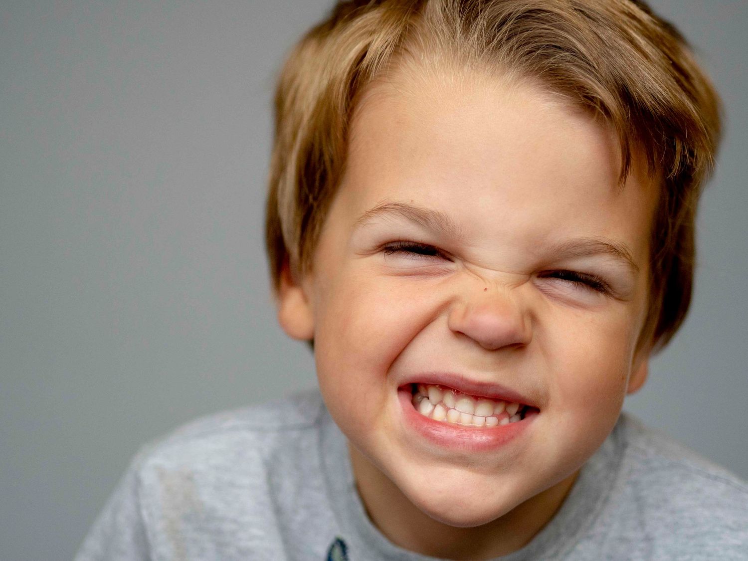 Pre-school aged boy, silly toothy smile, solid grey background.