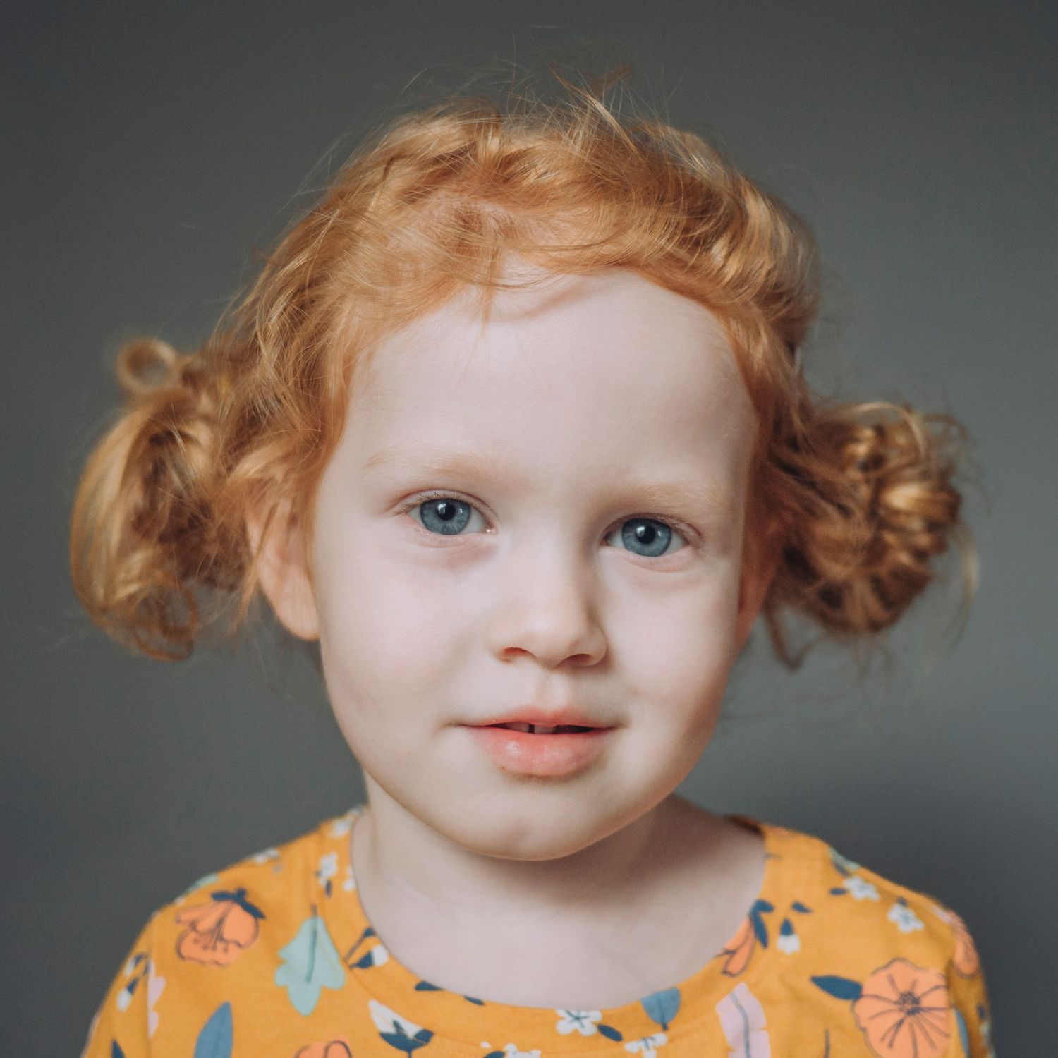 Pre-school aged girl, lovely red curly pigtails, slight smile,solid grey background.