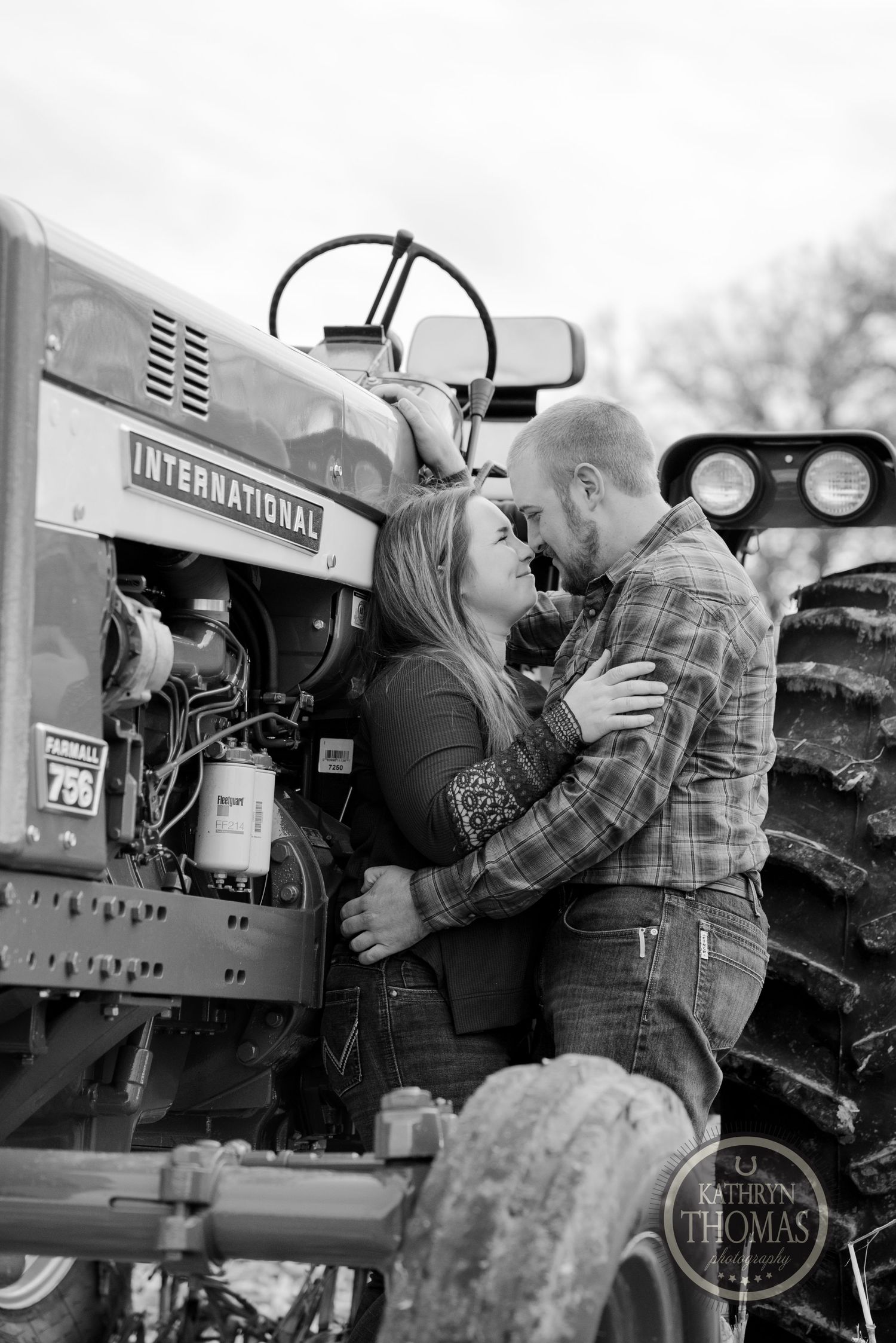 A couple shares an intimate moment on a classic International tractor in black and white.