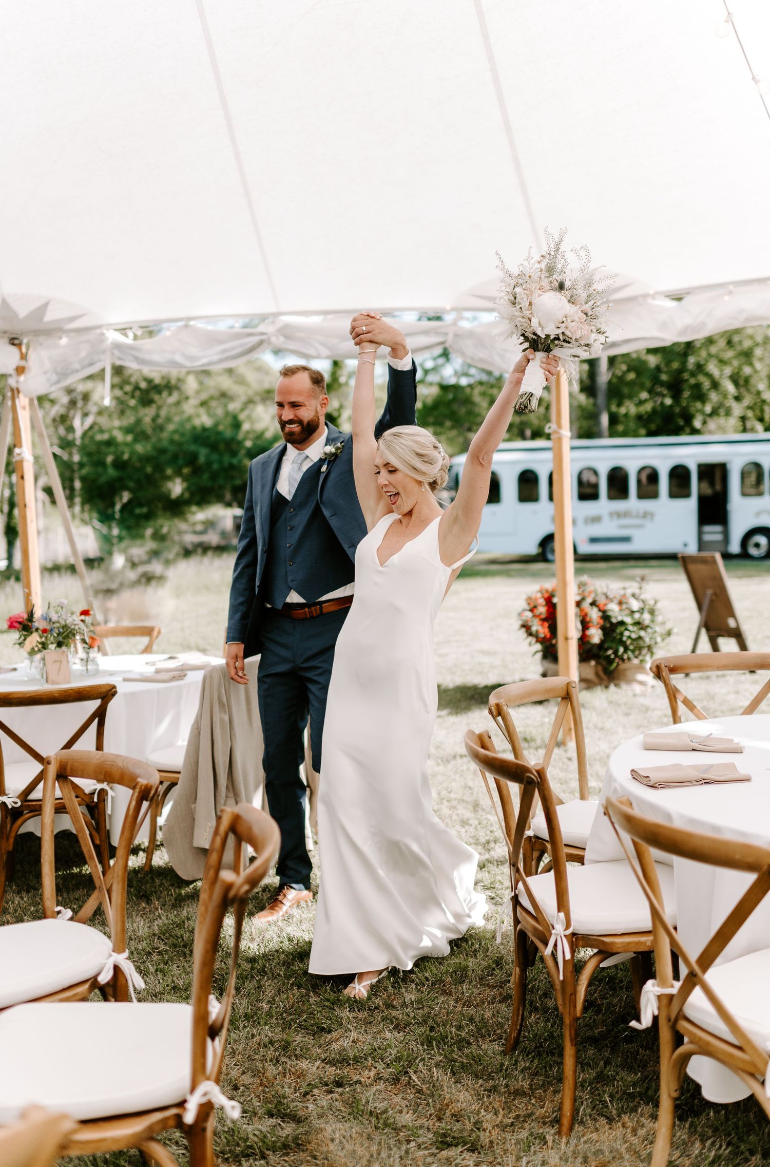 Joyful celebration moment under a white tent with rustic wooden chairs and elegant table settings.