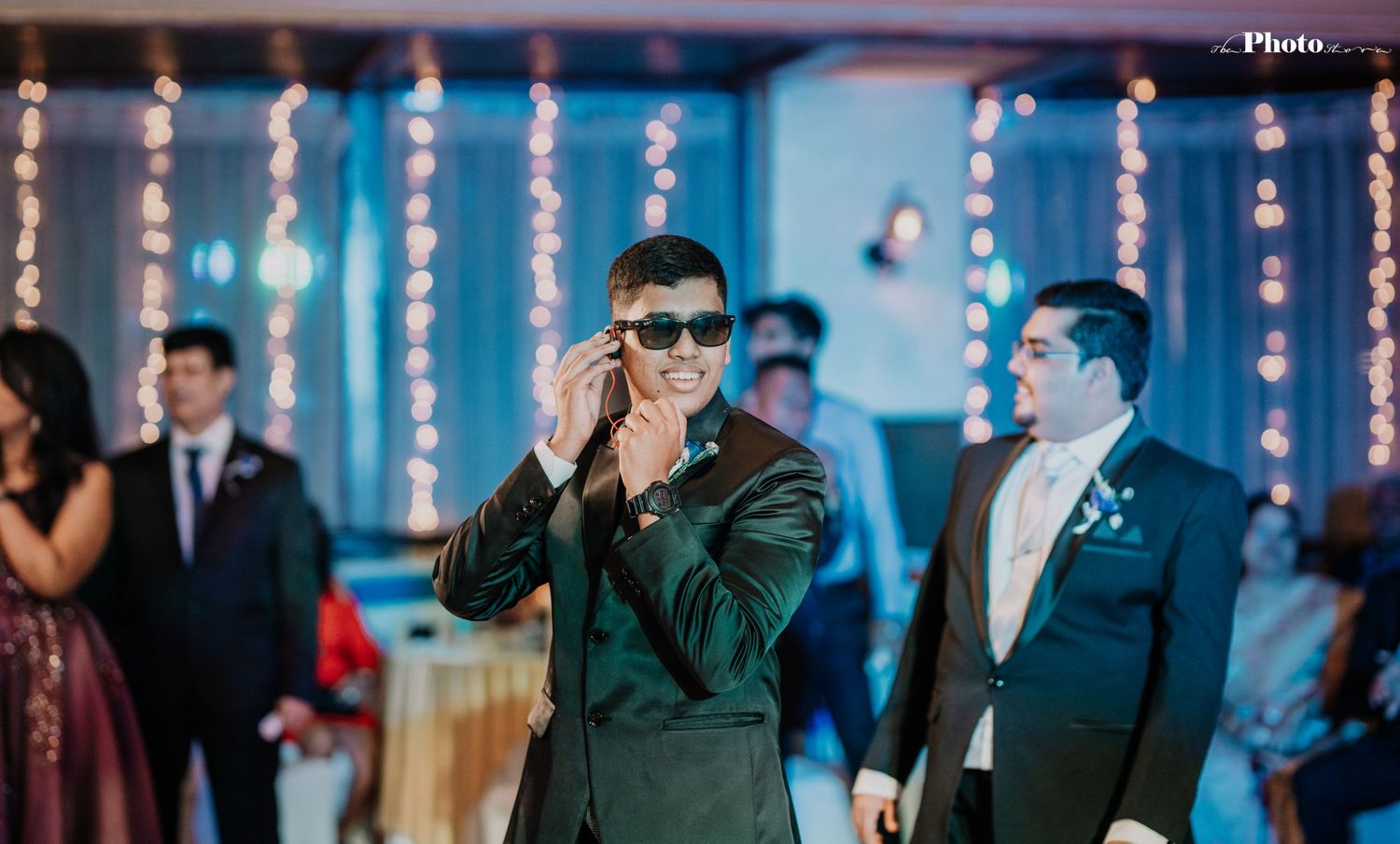 Wedding guests dancing and celebrating with sunglasses under blue lighting and string decorations.