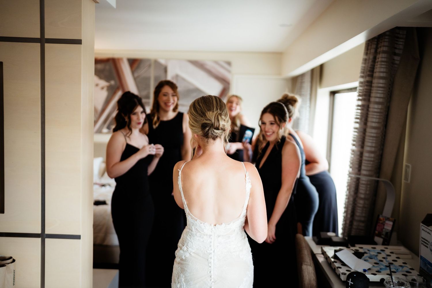 Wedding party in black dresses helping with bridal preparation.