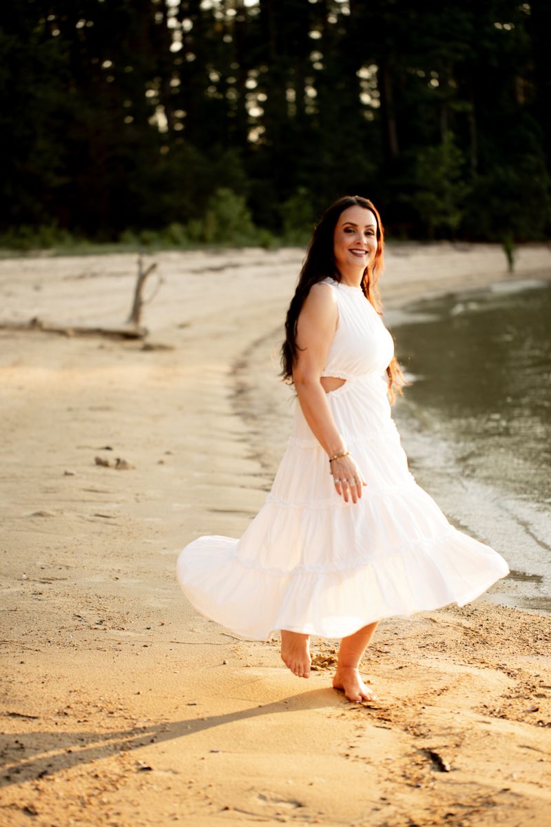 Woman in a white dress smiling and dancing on the shores of Clarks Hill Lake, SC.