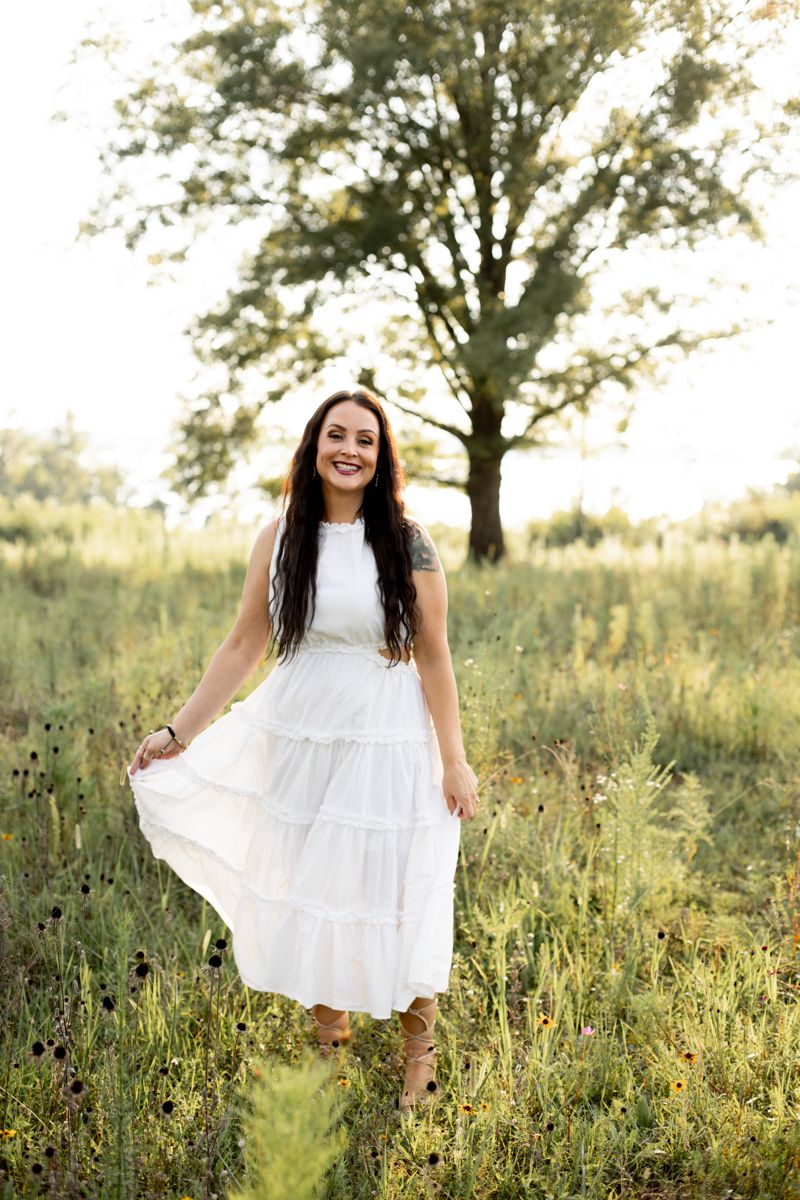 Woman in a white dress in a grassy field smiling at Clarks Hill, SC.