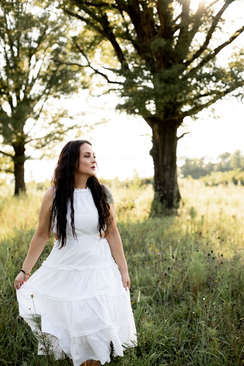Woman in white dress twirling her dress looking slightly off camera in Clarks Hill, SC field.