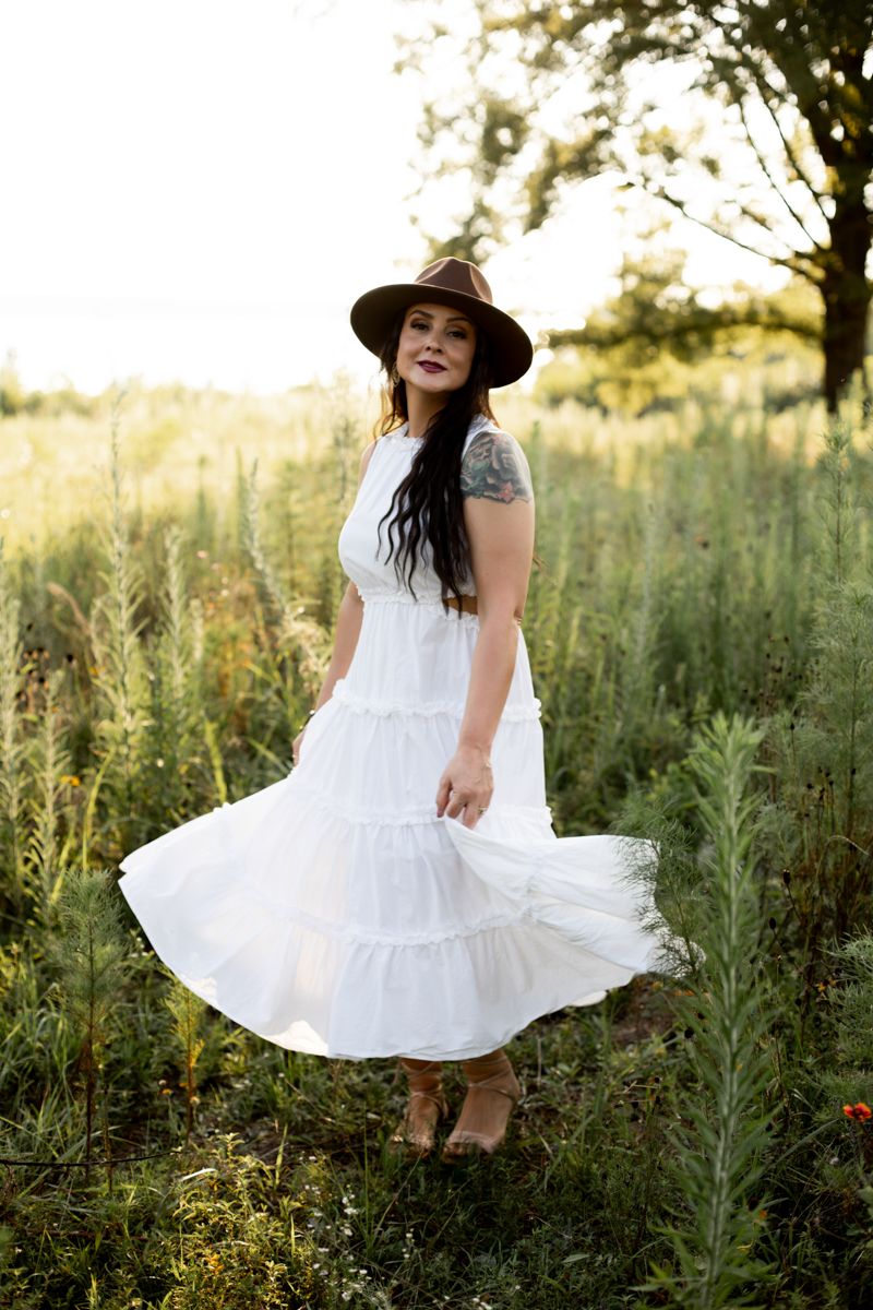 Woman in white dress in brown hat twirling in a grassy field in Clarks Hill, SC.