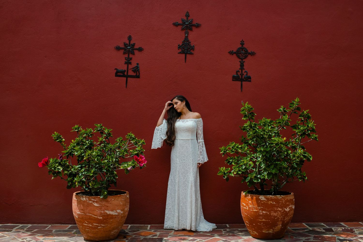 Wedding venue decorated with potted plants and crosses against rustic red wall.
