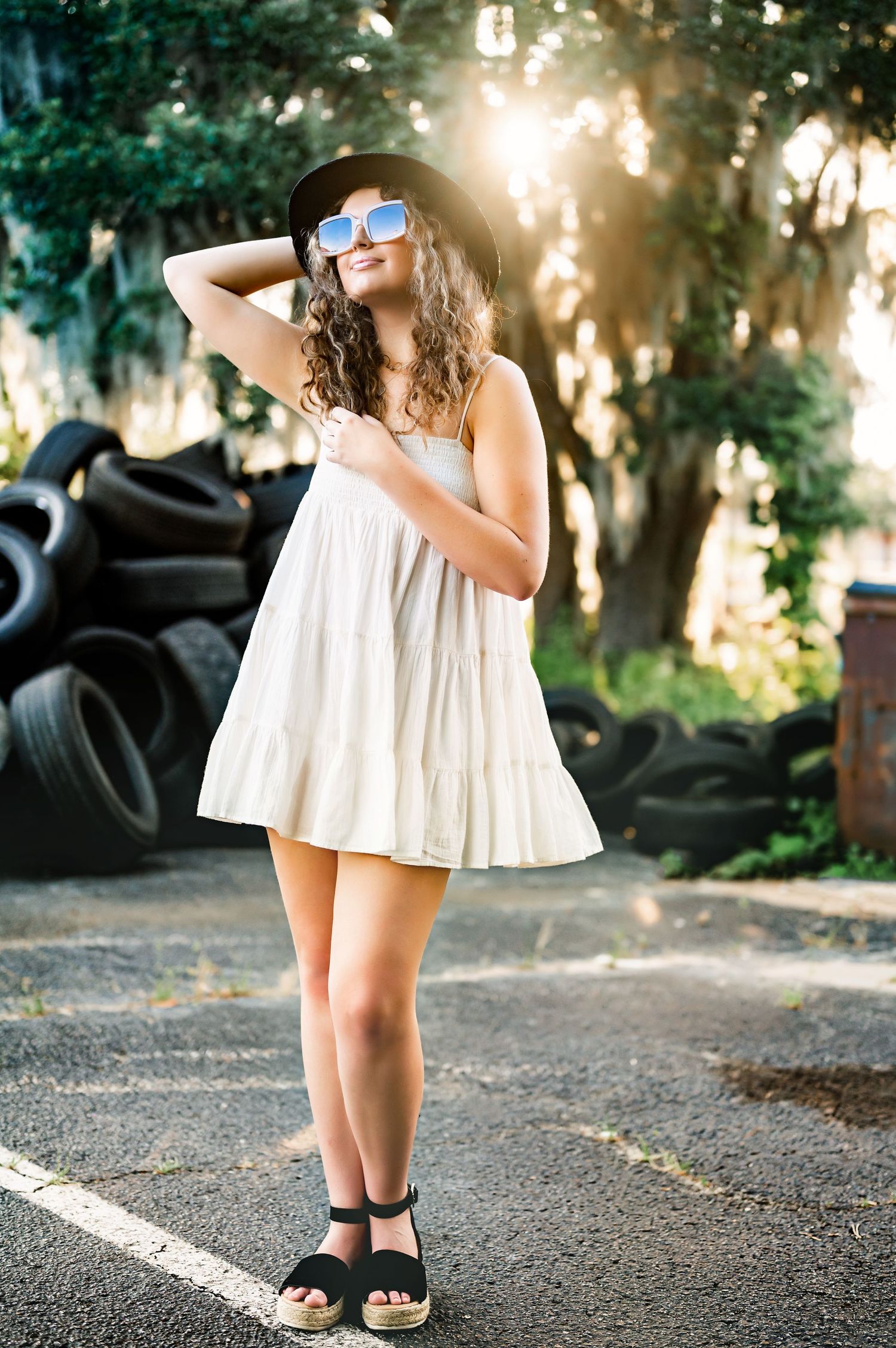 A summer fashion portrait with a flowing white dress and sunglasses in dappled sunlight.
