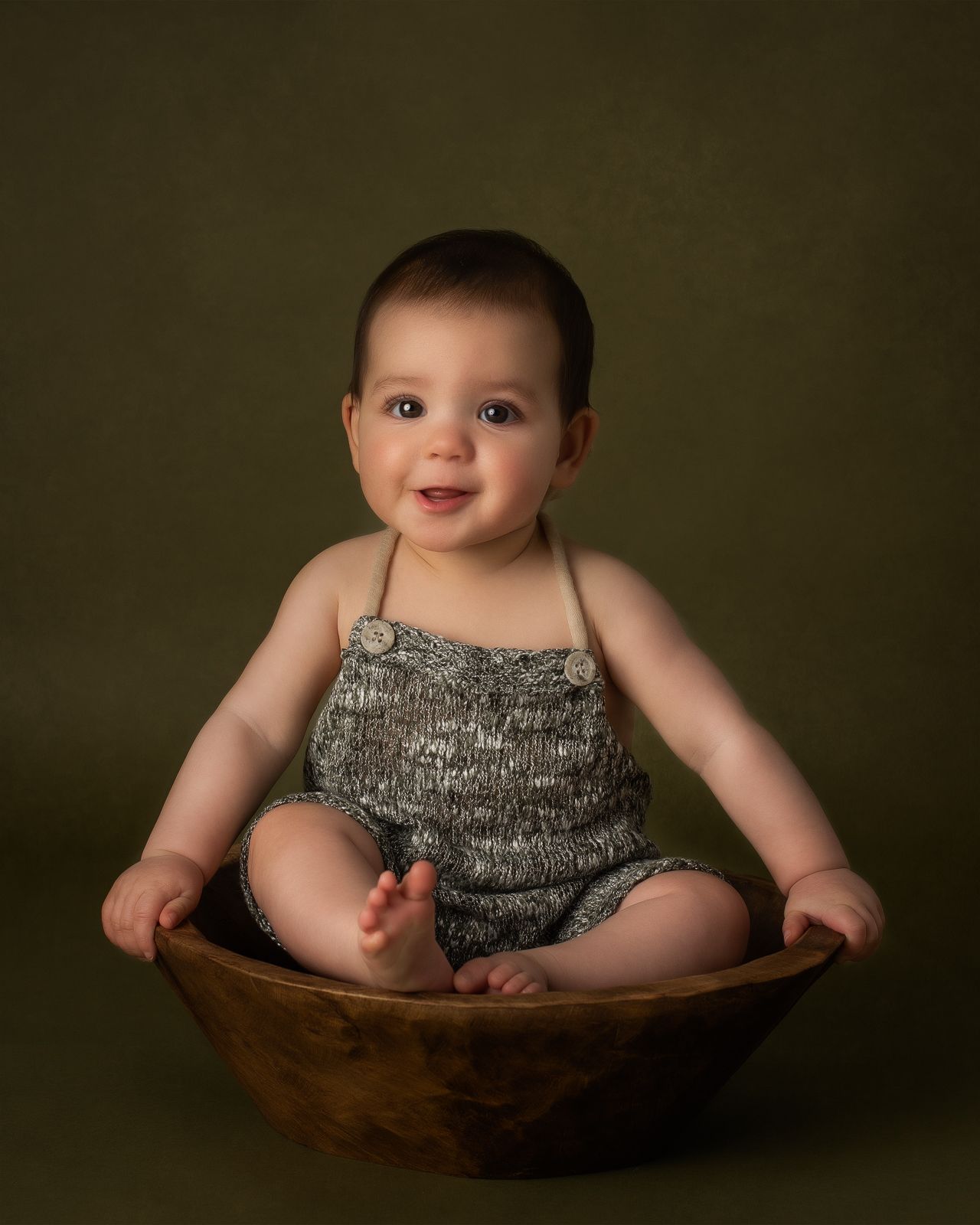 a baby wearing a knitted romper smiles for a milestone photographer