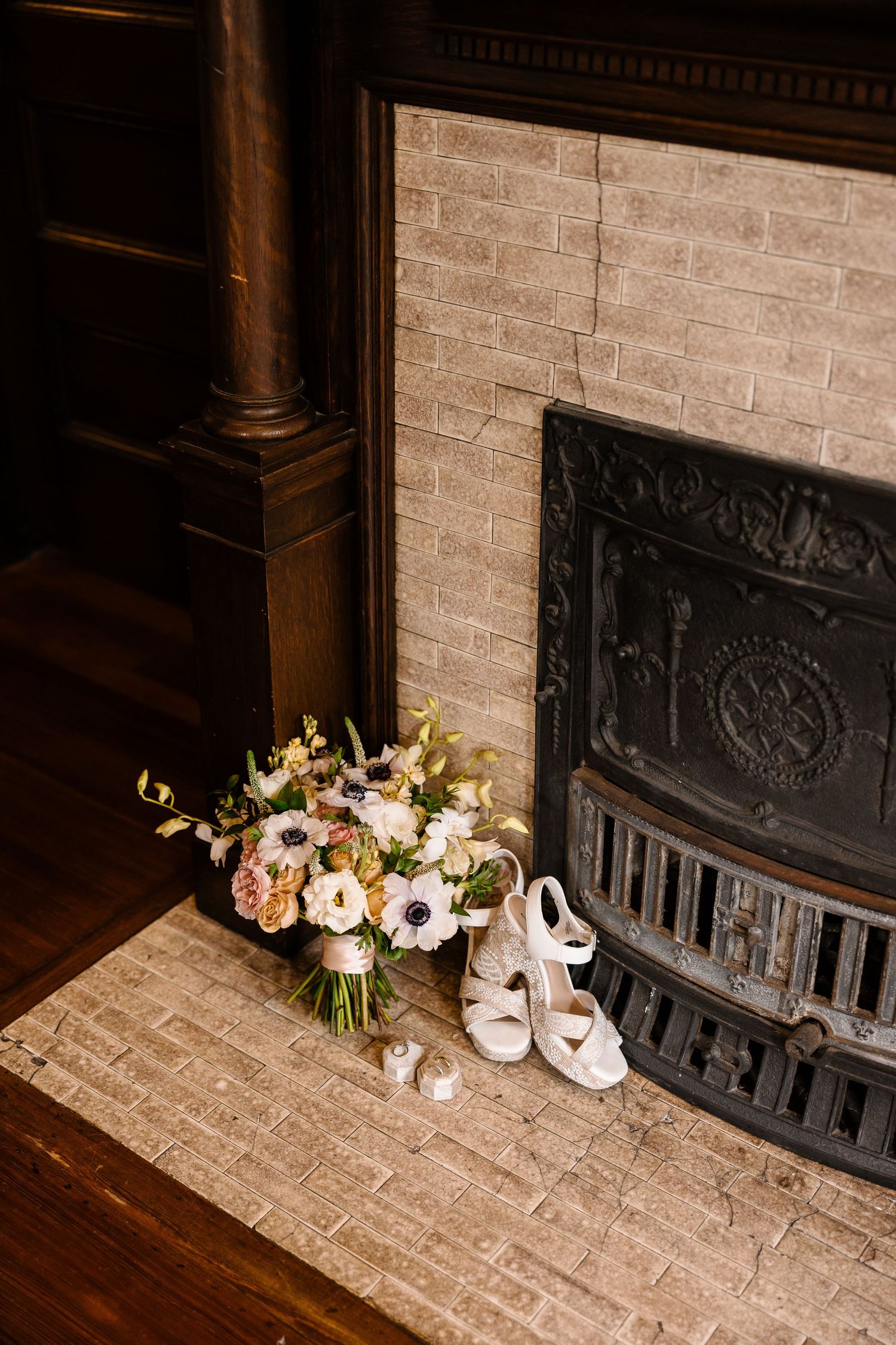 Bridal bouquet and white heeled shoes arranged beside a vintage fireplace on wedding day.