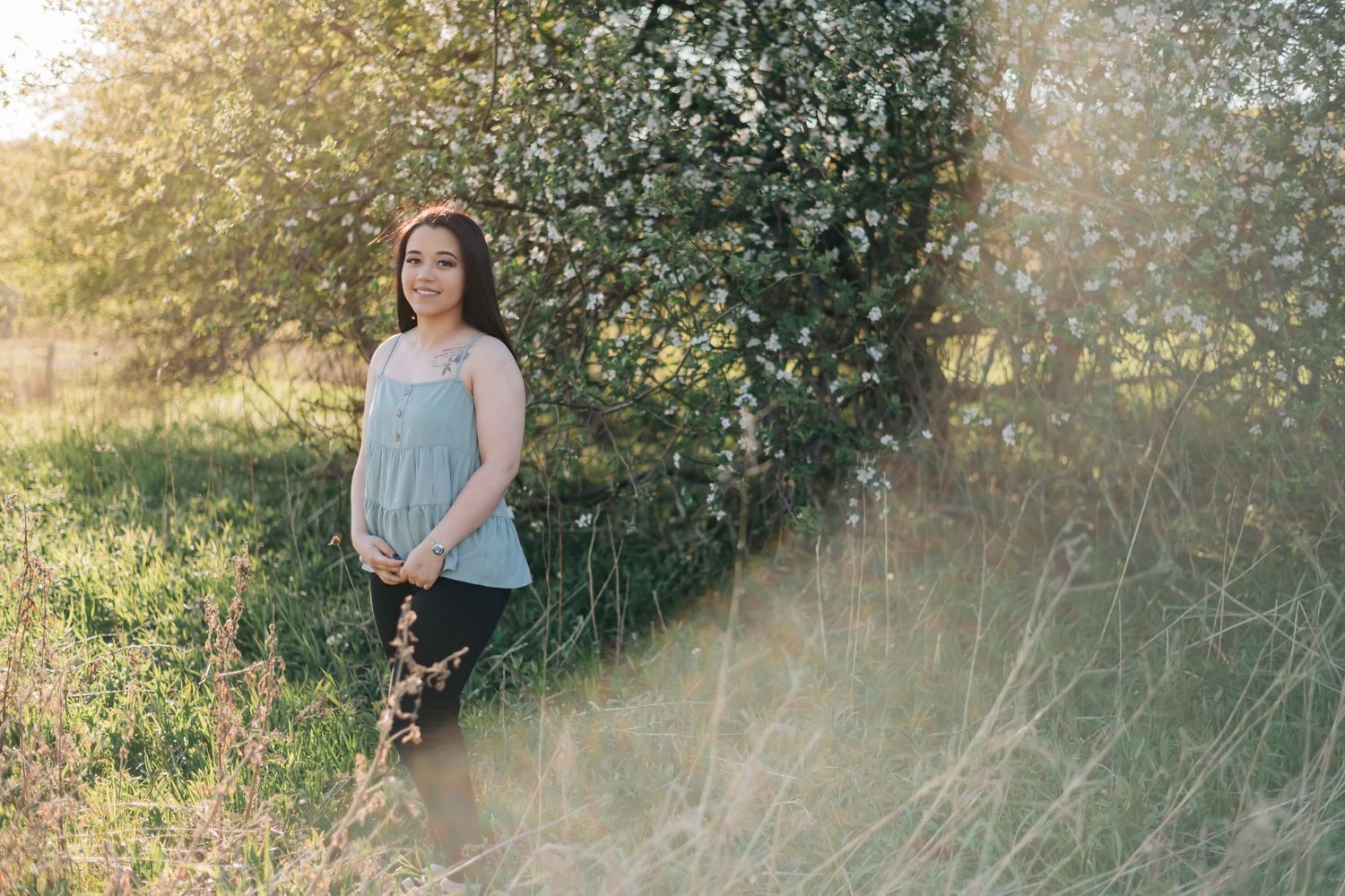 high school senior wearing a blue shirt standing in front of a blossoming apple tree