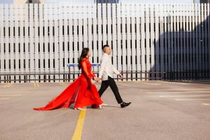 Dancing couple in red dress performing on outdoor patio with white fence backdrop.