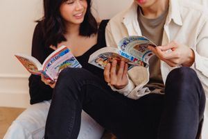 A couple sharing laughs while reading together in a casual indoor setting.