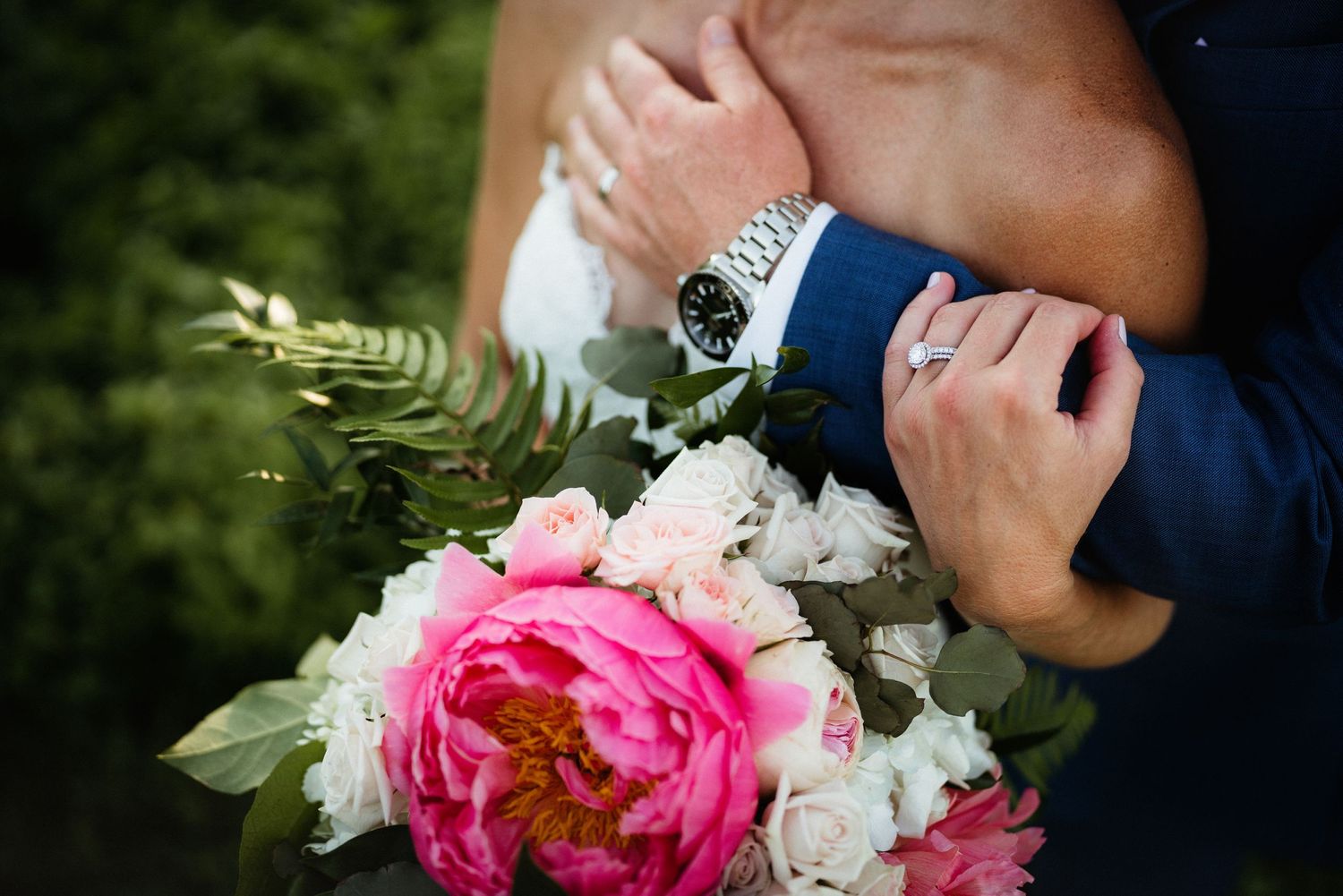 Close-up of wedding rings and a pink peony bouquet with white flowers and greenery.
